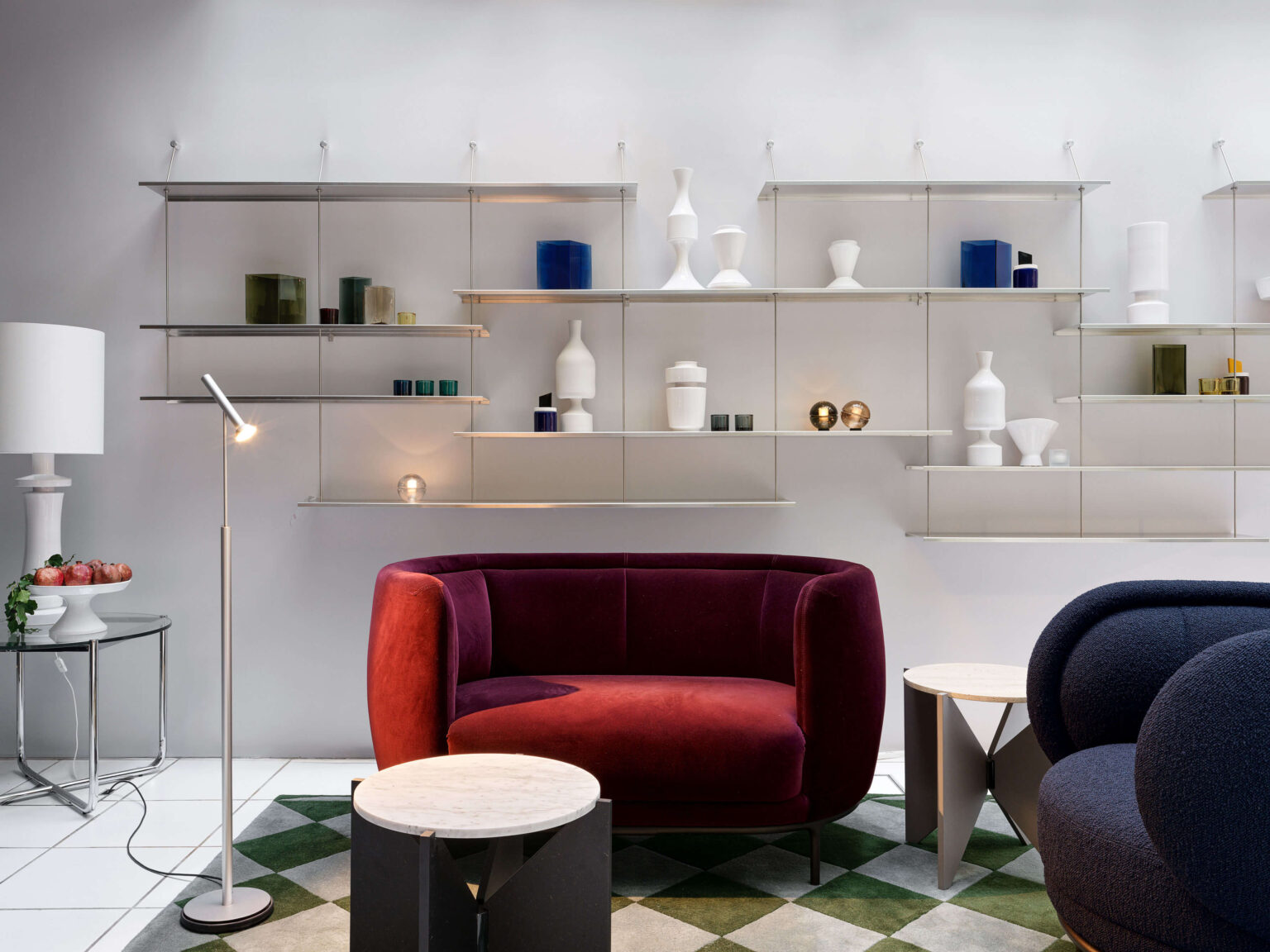 teo jakob Showroom in Bern mit rotem Sofa, runden Beistelltischen, filigranem Regalsystem an der Wand und dekorativen Vasen und Objekten.