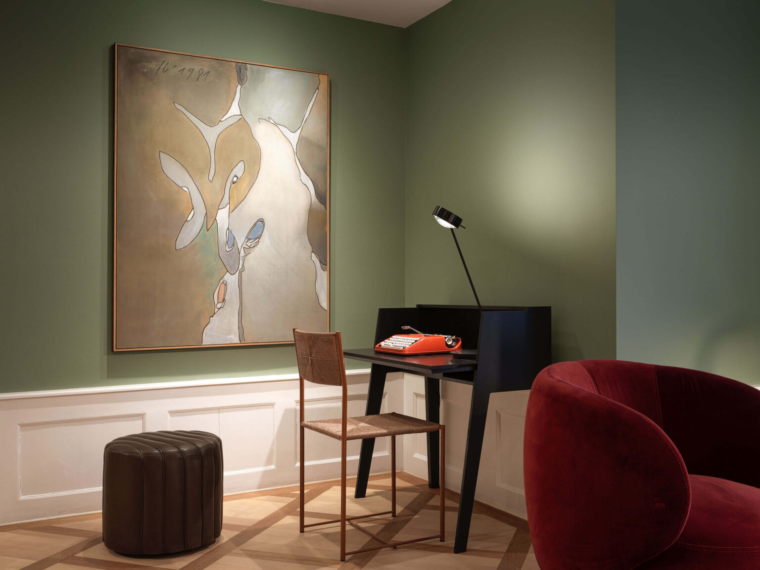 Grün gestrichener Occhio Light Space Showroom bei teo jakob Bern, mit grossem Kunstwerk, kleinem schwarzen Sekretär, roter Schreibmaschine, Stuhl und rotem Sessel.