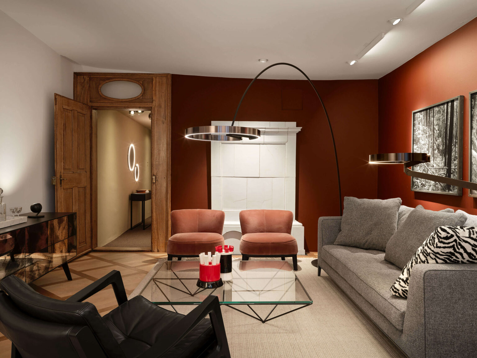 Occhio Light Space Showroom bei teo jakob Bern, mit roten Wänden, grauem Sofa, zwei rosafarbenen Sesseln, Glastisch und grossen bogenförmigen Leuchten von Occhio.