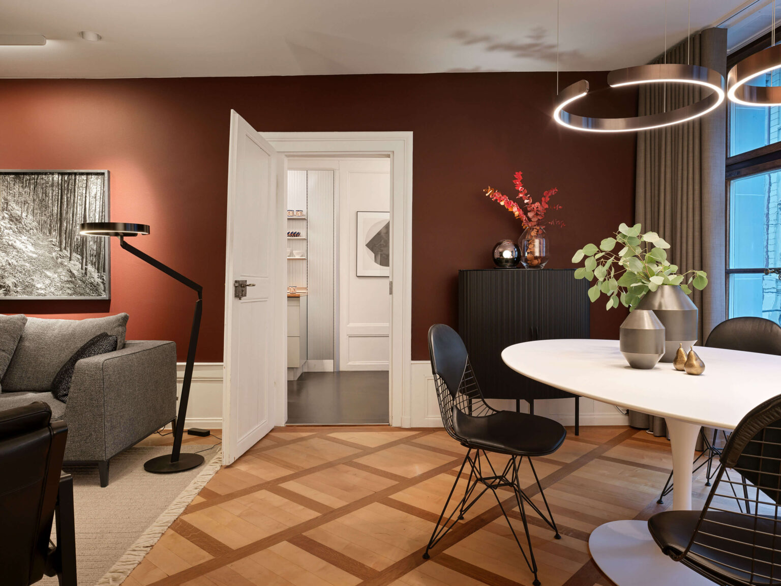Occhio Light Space Showroom, teo jakob Bern, mit dunkler, rotbrauner Wand, weissem Esstisch, schwarzen Stühlen, dekorativen Vasen und ringförmigen Pendelleuchten von Occhio.