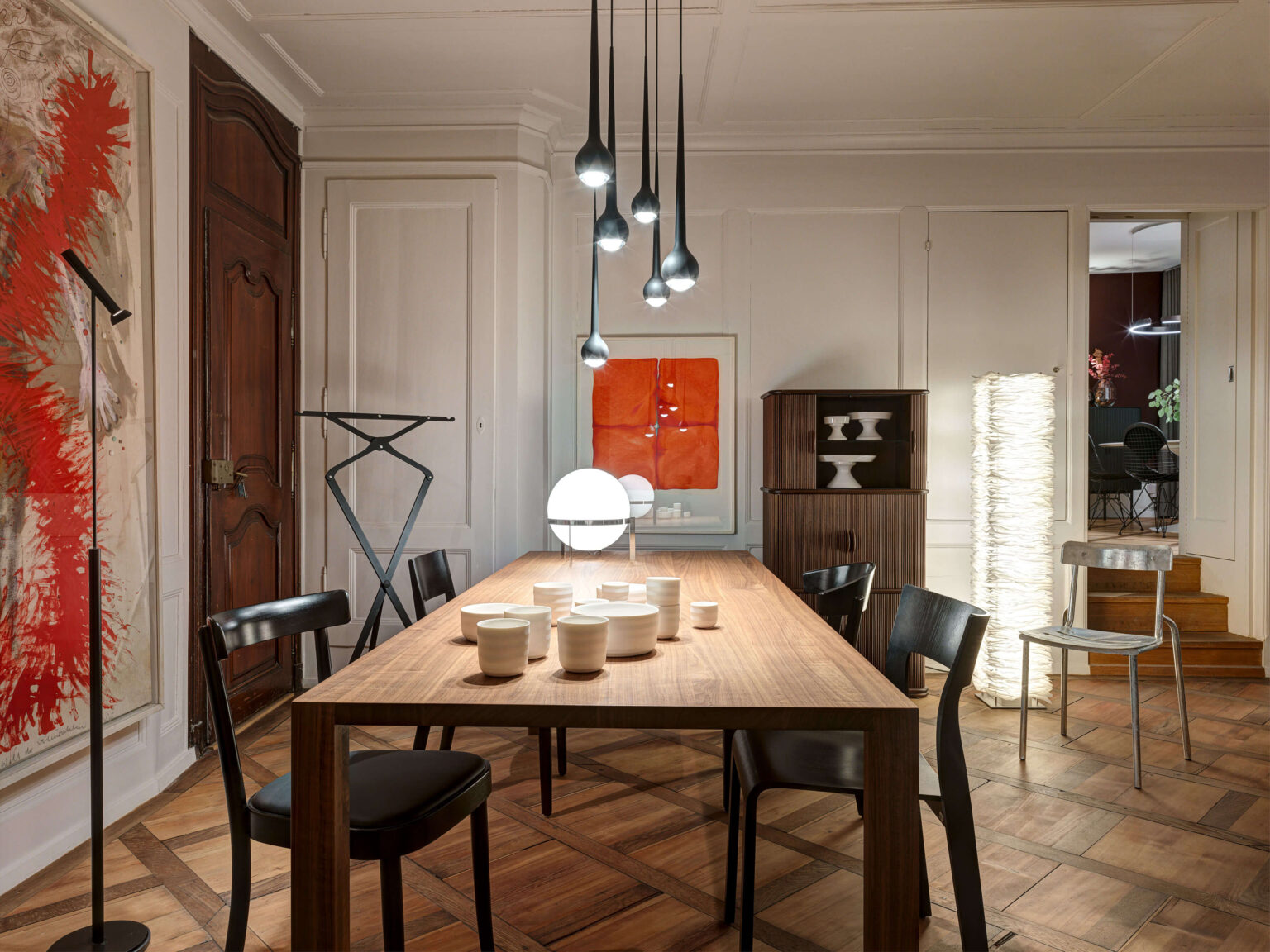 Innenansicht des teo jakob Showrooms in Bern mit langem Holztisch, schwarzen Stühlen, mehreren hängenden Pendelleuchten, Kunstwerken an den Wänden und wohnlicher Einrichtung.