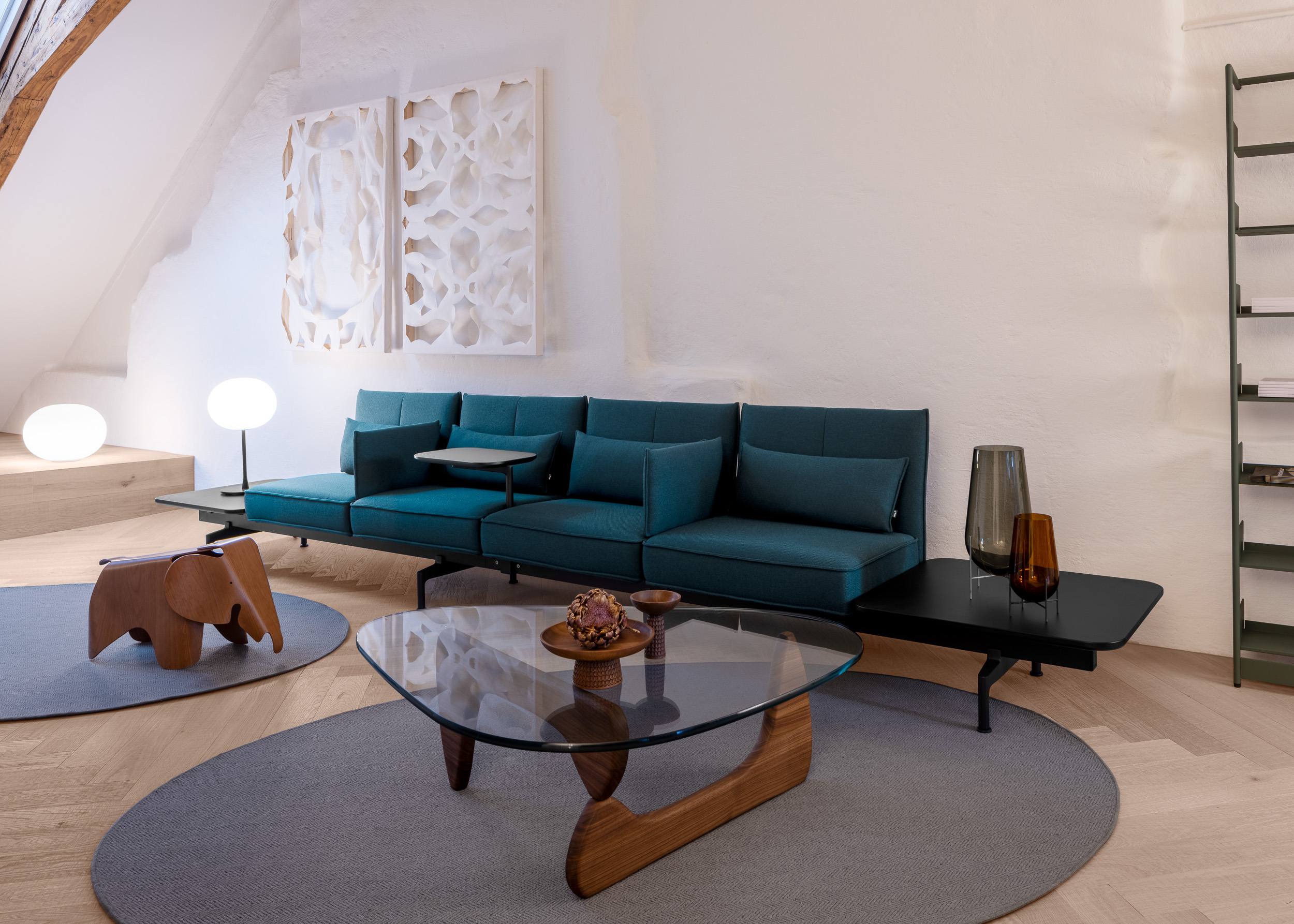 Lounge im Loft: türkisfarbene Sofalandschaft, Glas-Couchtisch mit Holzgestell, zwei opale Kugelleuchten und skulpturale Wandreliefs.