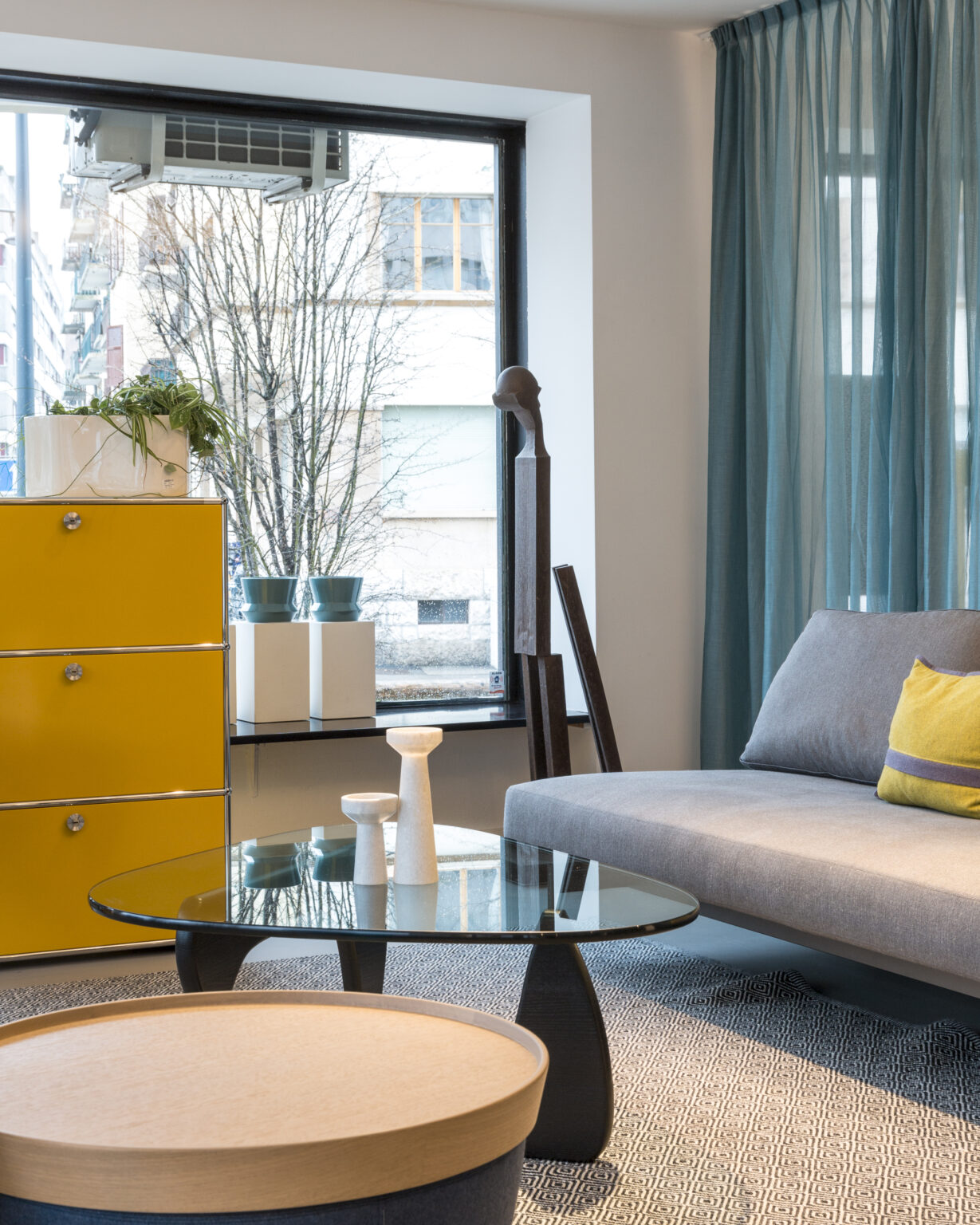 Wohninszenierung im Showroom teo jakob Genf mit Sofa, Glastisch und farbigem Sideboard.