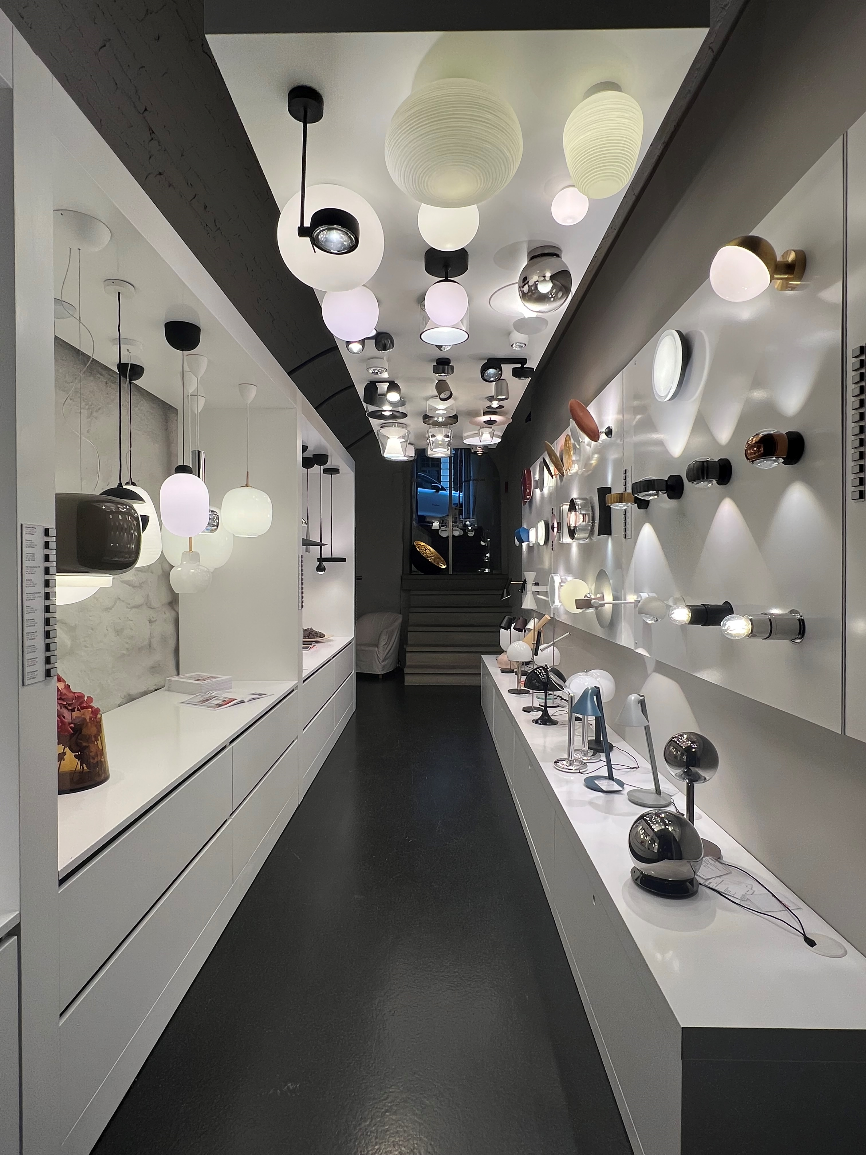 Showroom-Gang im Leuchtenkeller Bern mit bestückter Decke und Wänden voller Leuchten—Kugel-, Spot- und Wandleuchten—sowie Tischlampen.