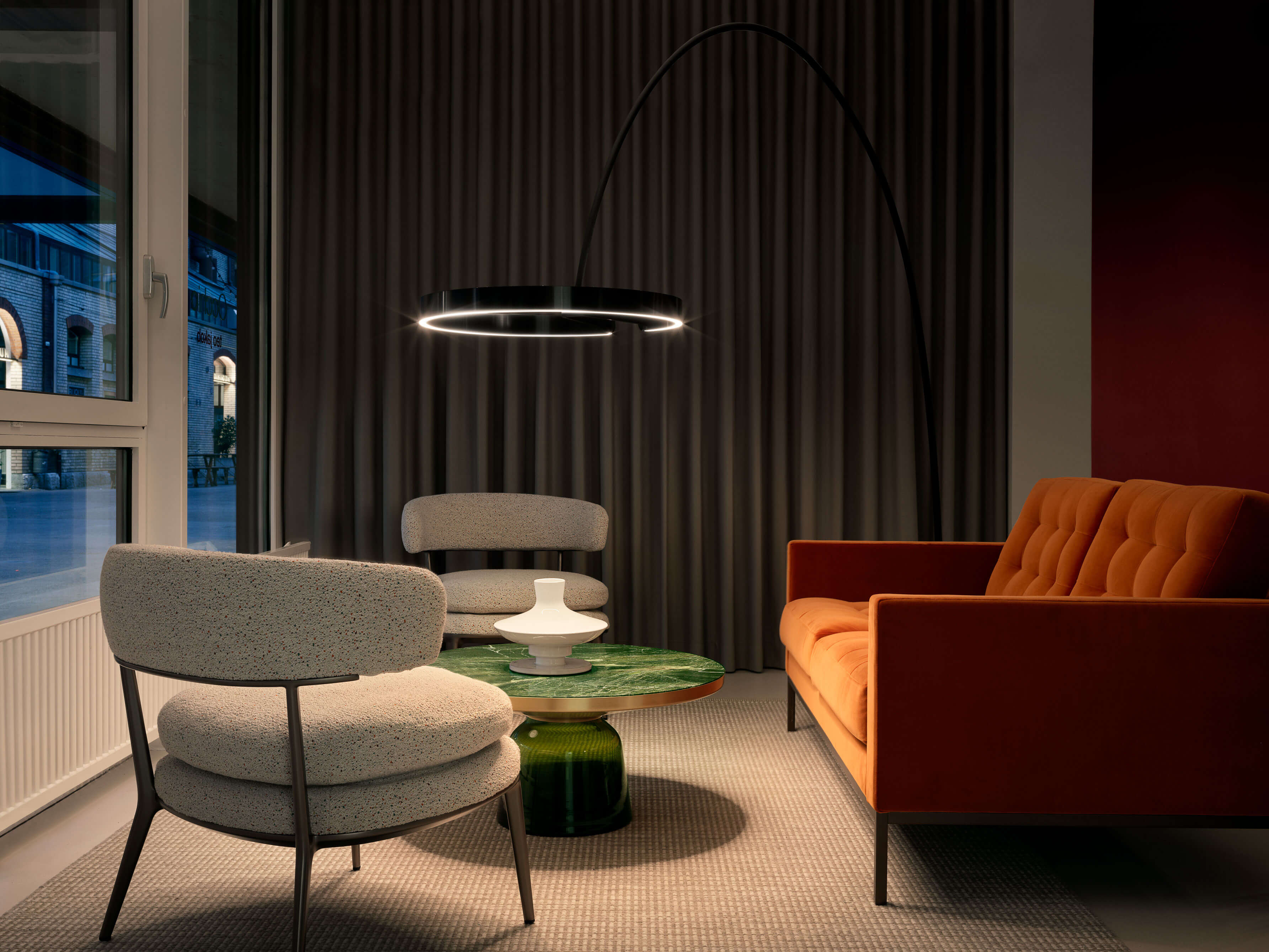 Lounge mit orangefarbenem Sofa, zwei hellen Sesseln, grünem Marmortisch und grossem bogenförmigem Ringlicht.