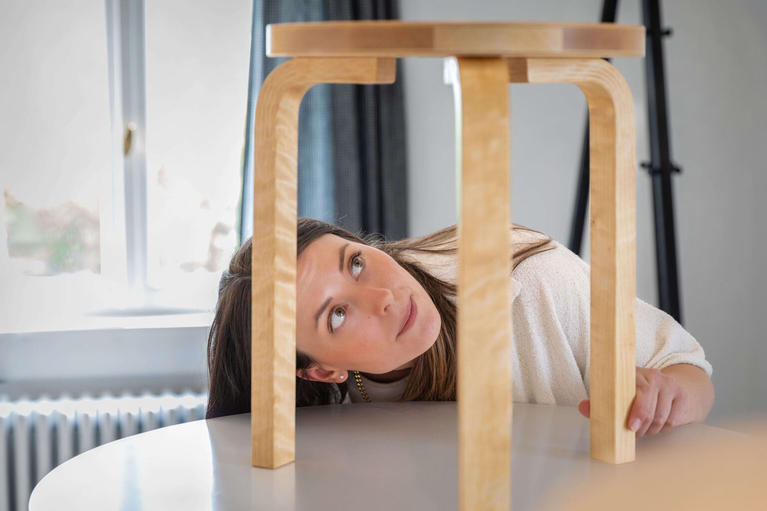 Frau betrachtet Holzhocker von unten auf Tisch.