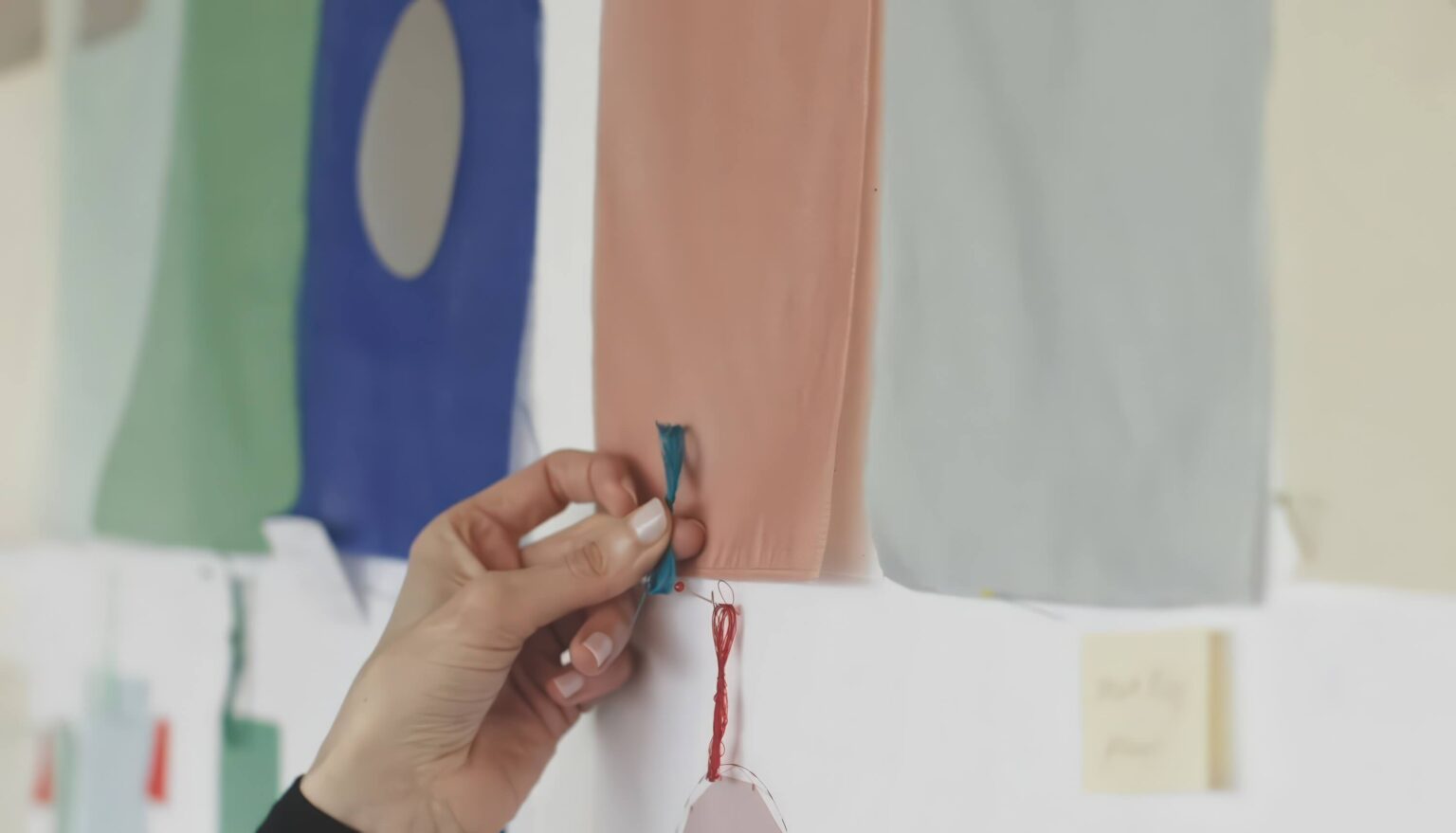 Hand prüft Stoffmuster in verschiedenen Farben an Wand.