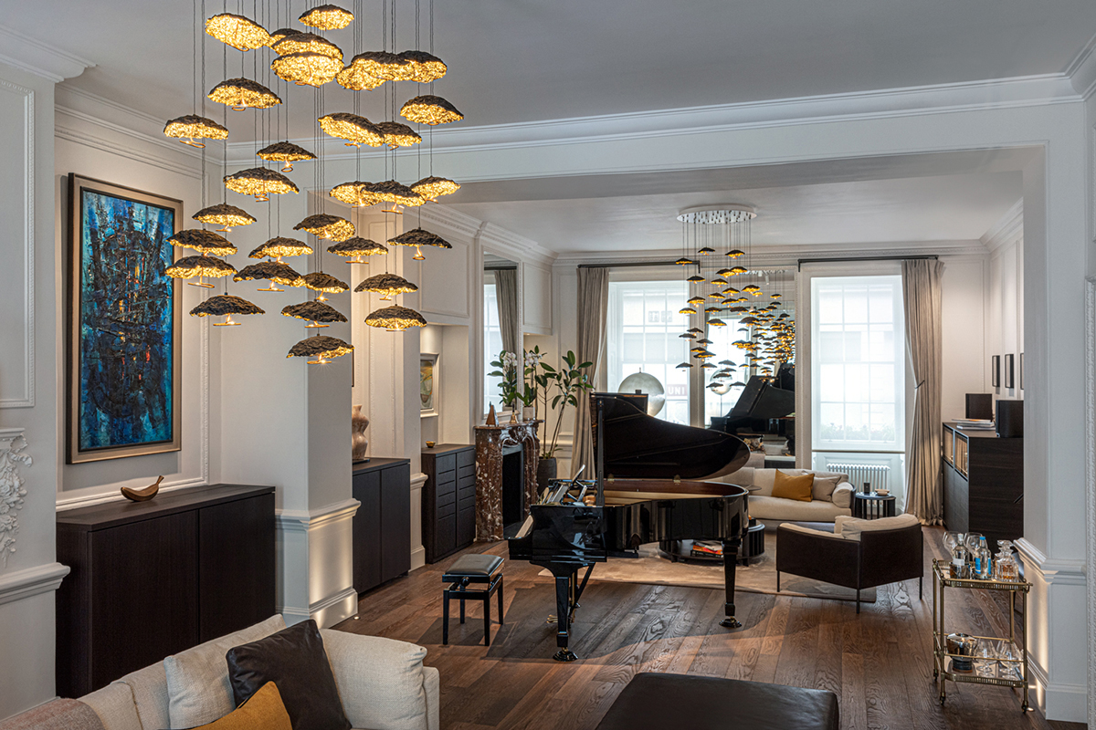 Elegantes Wohnzimmer mit vielen goldfarbenen Hängeleuchten, schwarzem Flügel im Zentrum, hellen Sitzmöbeln, grossen Fenstern und dunklem Holzboden.