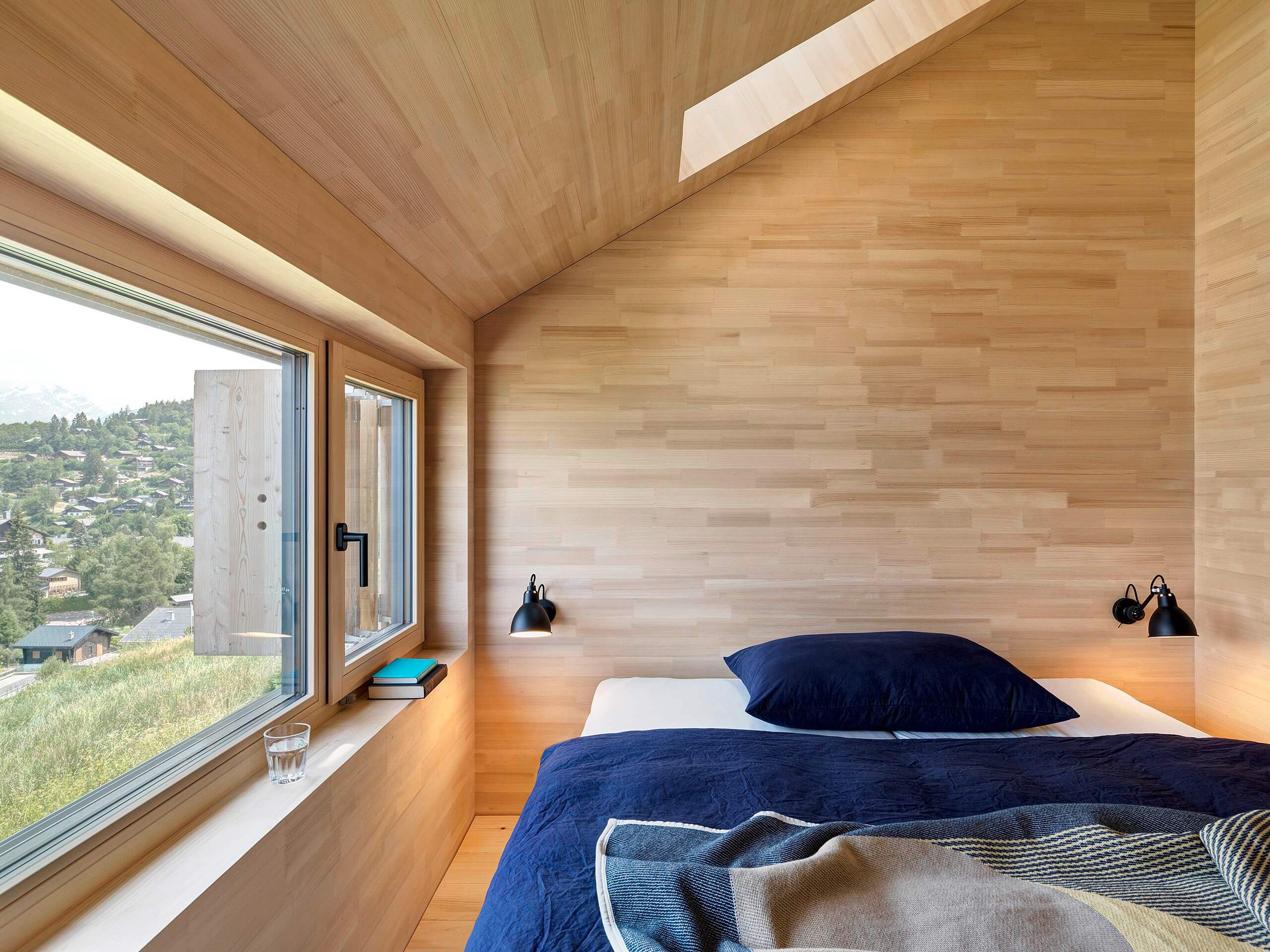 Schlafzimmer mit grossem Fenster und Oberlicht, komplett in hellem Holz gestaltet, mit Ausblick über Vercorin und die Berglandschaft.