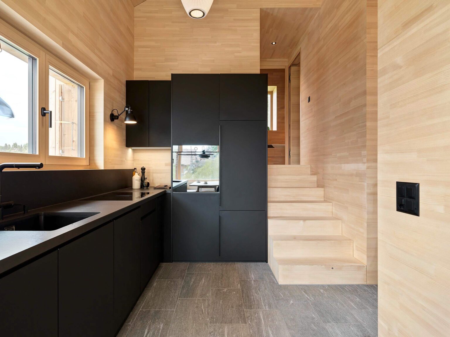 Küche mit mattschwarzen Fronten und integrierten Geräten, kombiniert mit Holzverkleidung und Steinboden, im Ferienhaus in Vercorin.