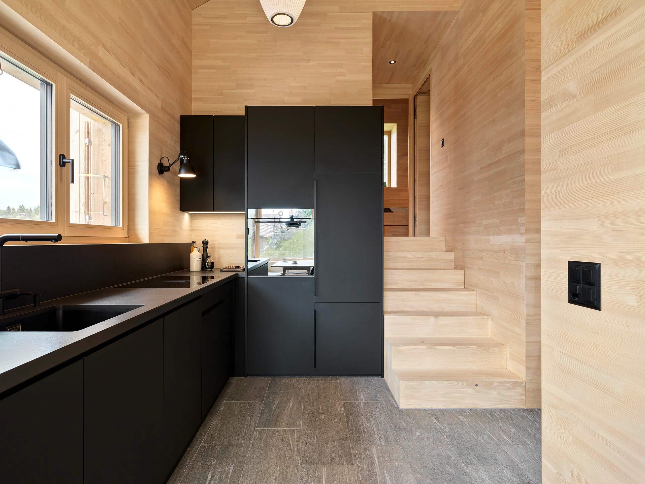 Küche mit mattschwarzen Fronten und integrierten Geräten, kombiniert mit Holzverkleidung und Steinboden, im Ferienhaus in Vercorin.