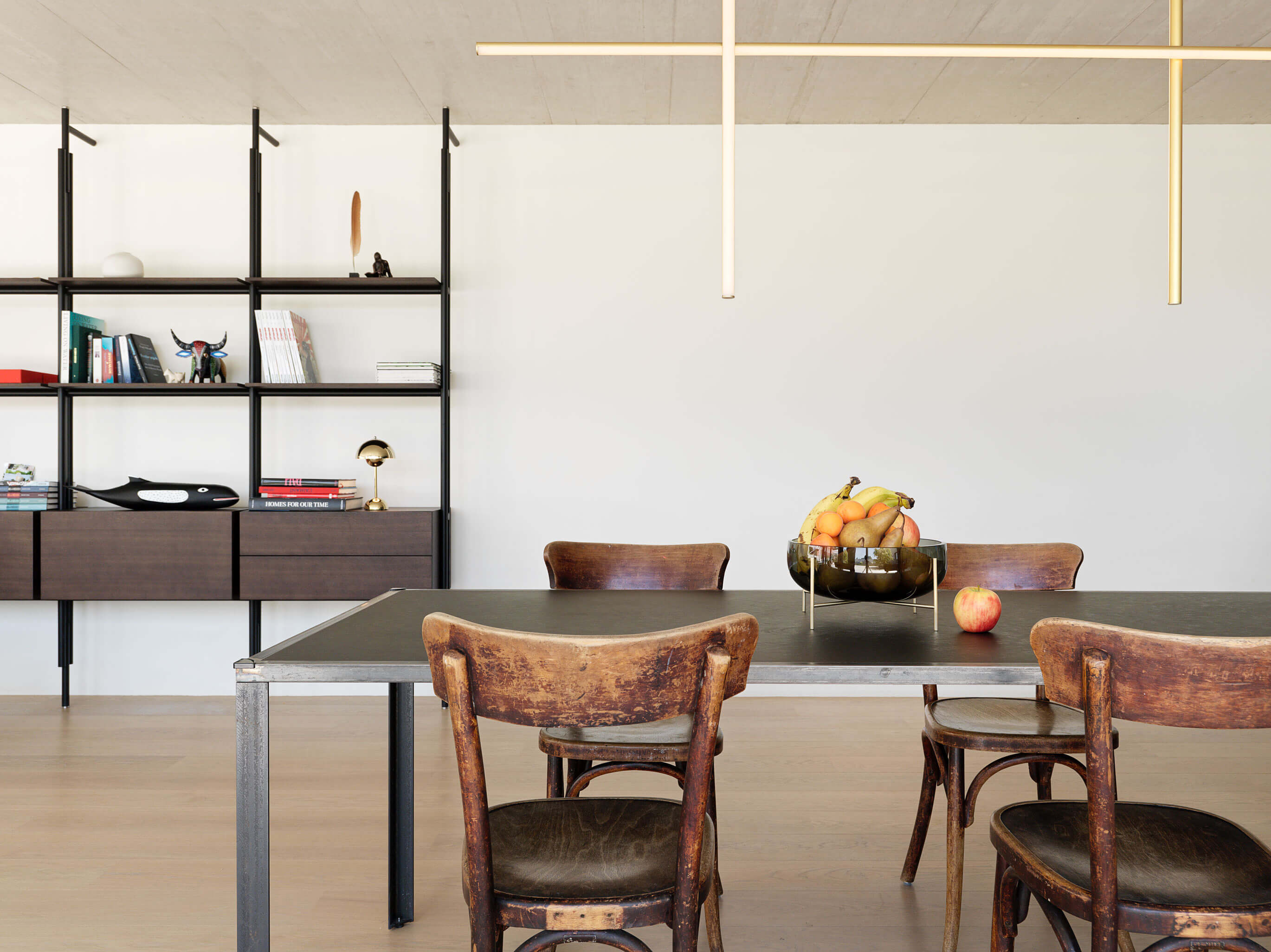 Essbereich eines Patiohauses in Winterthur mit linearem Pendellicht, schwarzem Regalsystem, Holztisch und Vintage-Stühlen.