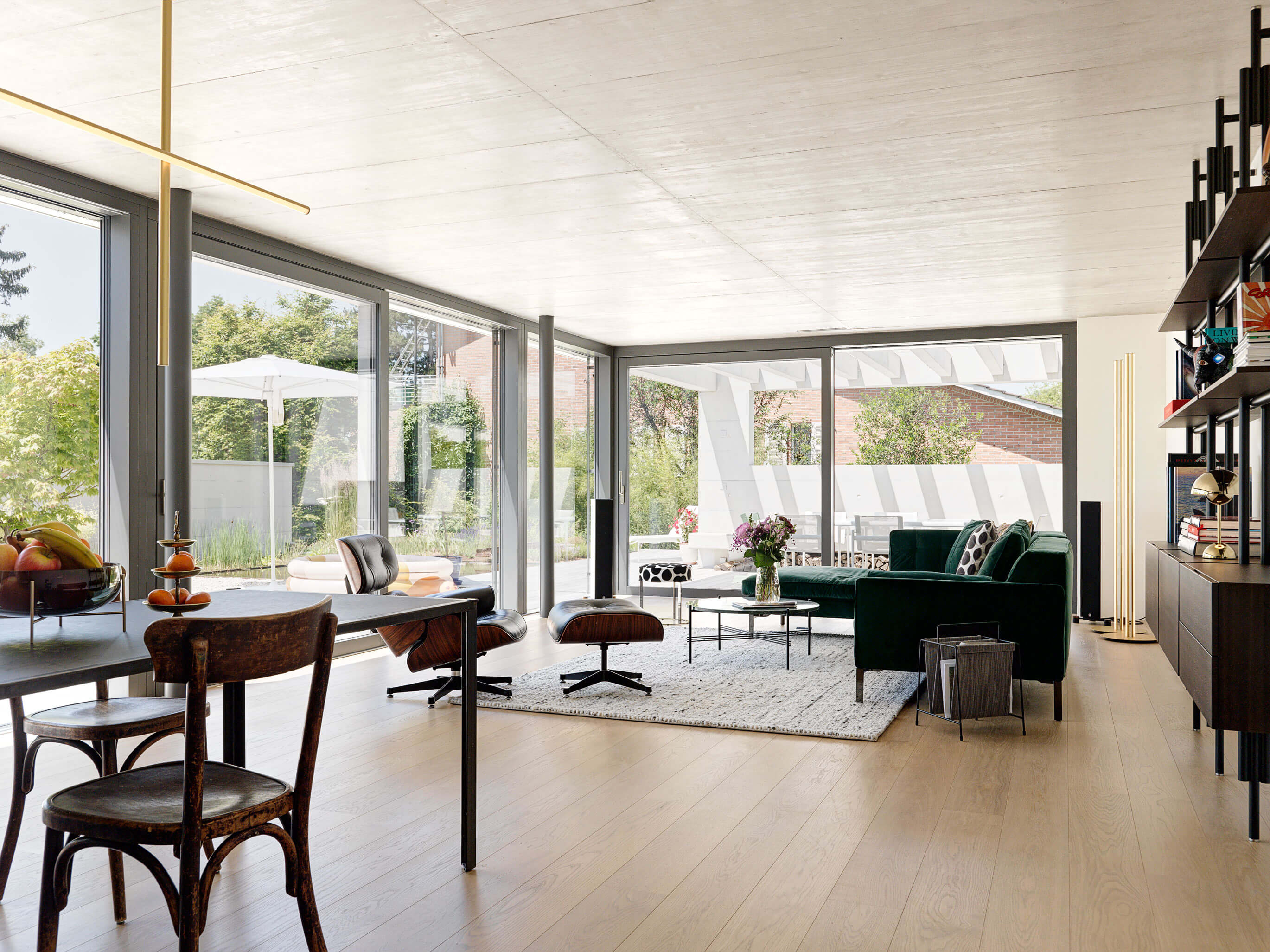 Offener Wohn- und Essbereich eines Patiohauses in Winterthur mit grossen Schiebetüren zum Patio, grüner Sofa-Lounge und Blick in den Garten.