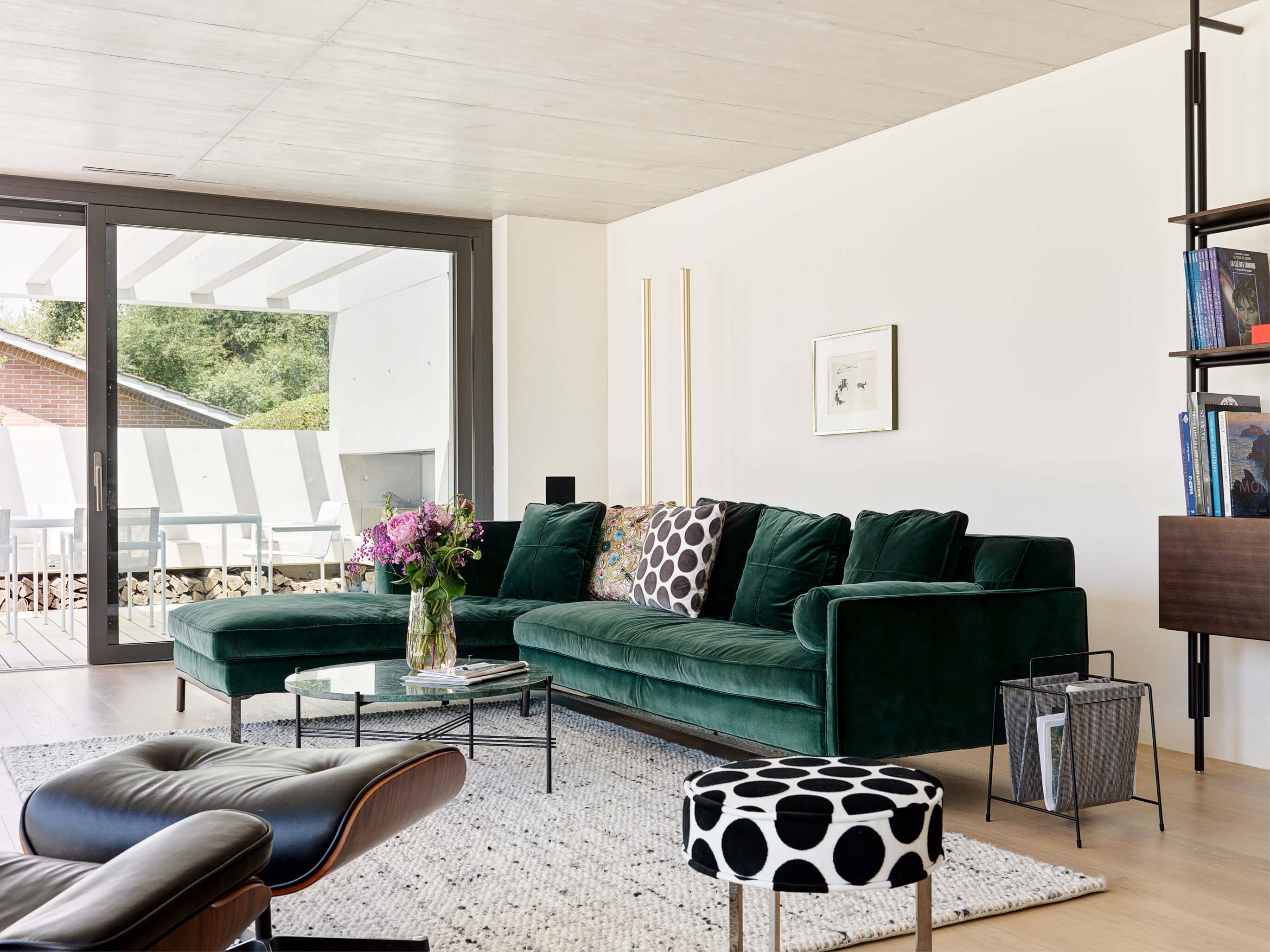 Weiter Blick in den offenen Wohn-/Essbereich mit grüner Eckcouch, großem Schiebetürfenster zum Patio und hellem Teppich, im Patiohaus in Winterthur.