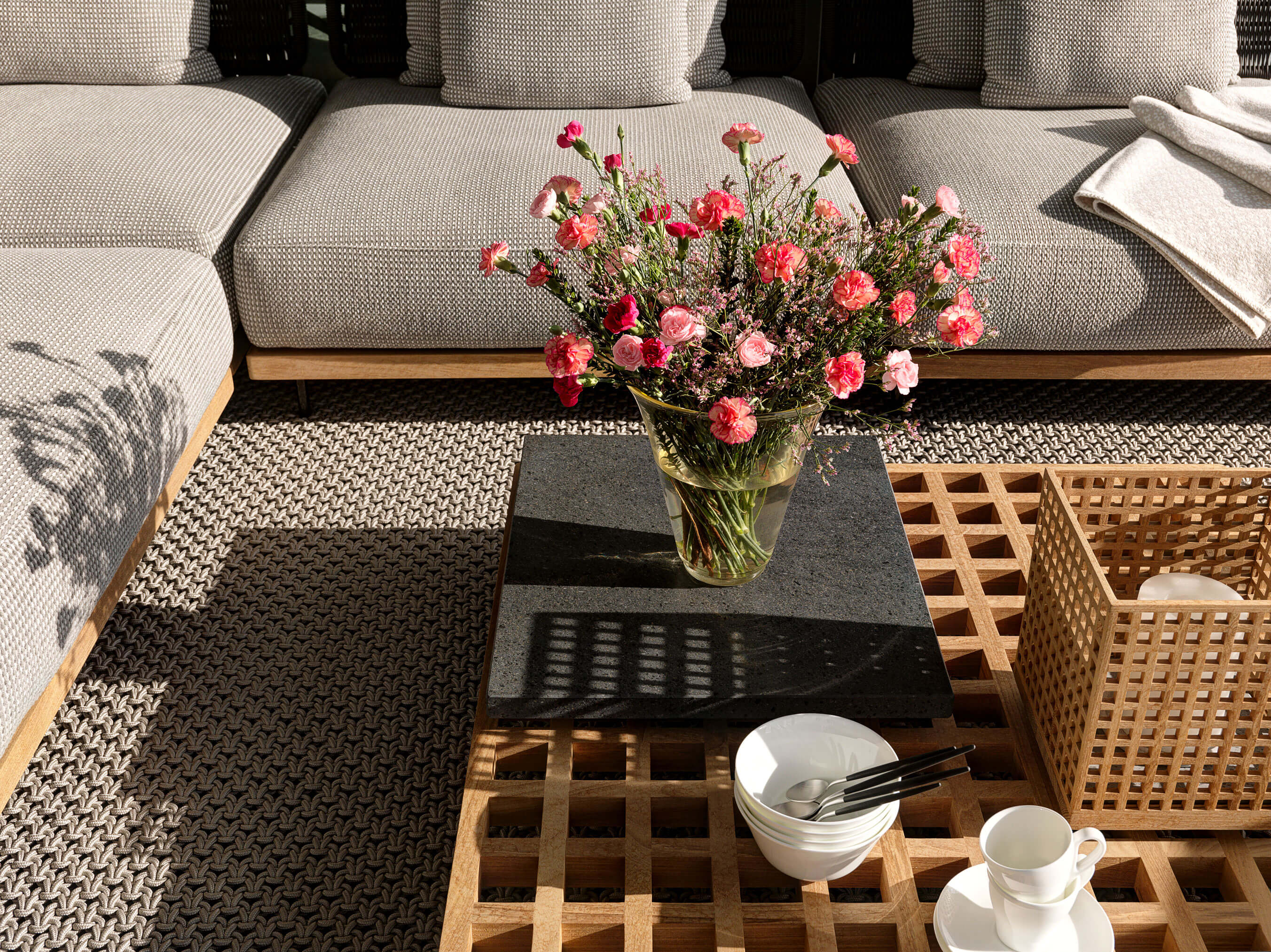 Holzgitter-Tisch mit Blumenstrauss, Schalen und geflochtenem Outdoor-Teppich in einer Stadtwohnung in Zug.