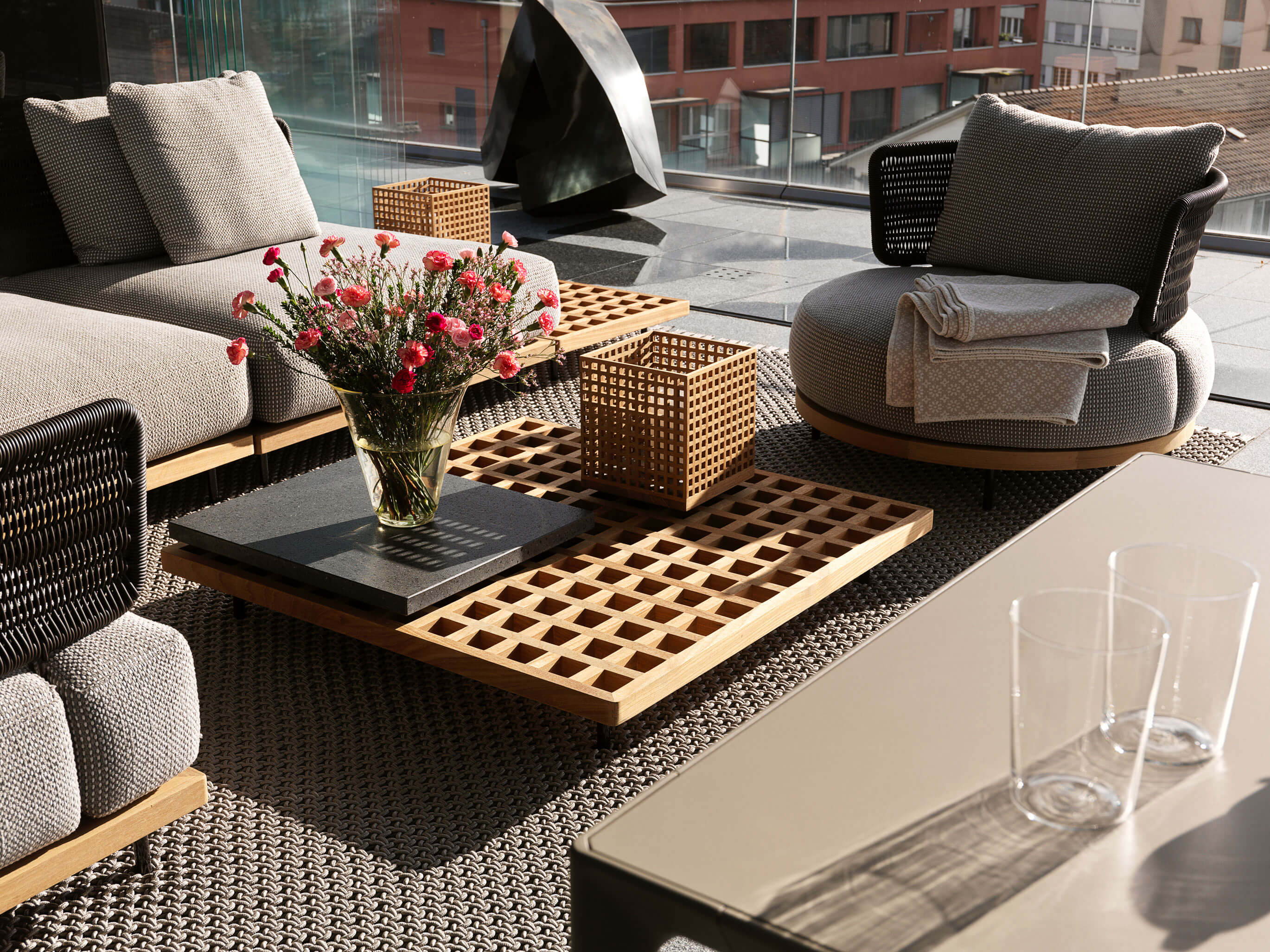 Terrasse der Stadtwohnung beim Bahnhof Zug mit Lounge-Ensemble, Holz-Gittertisch und Glasbrüstung mit Blick über die Stadt.