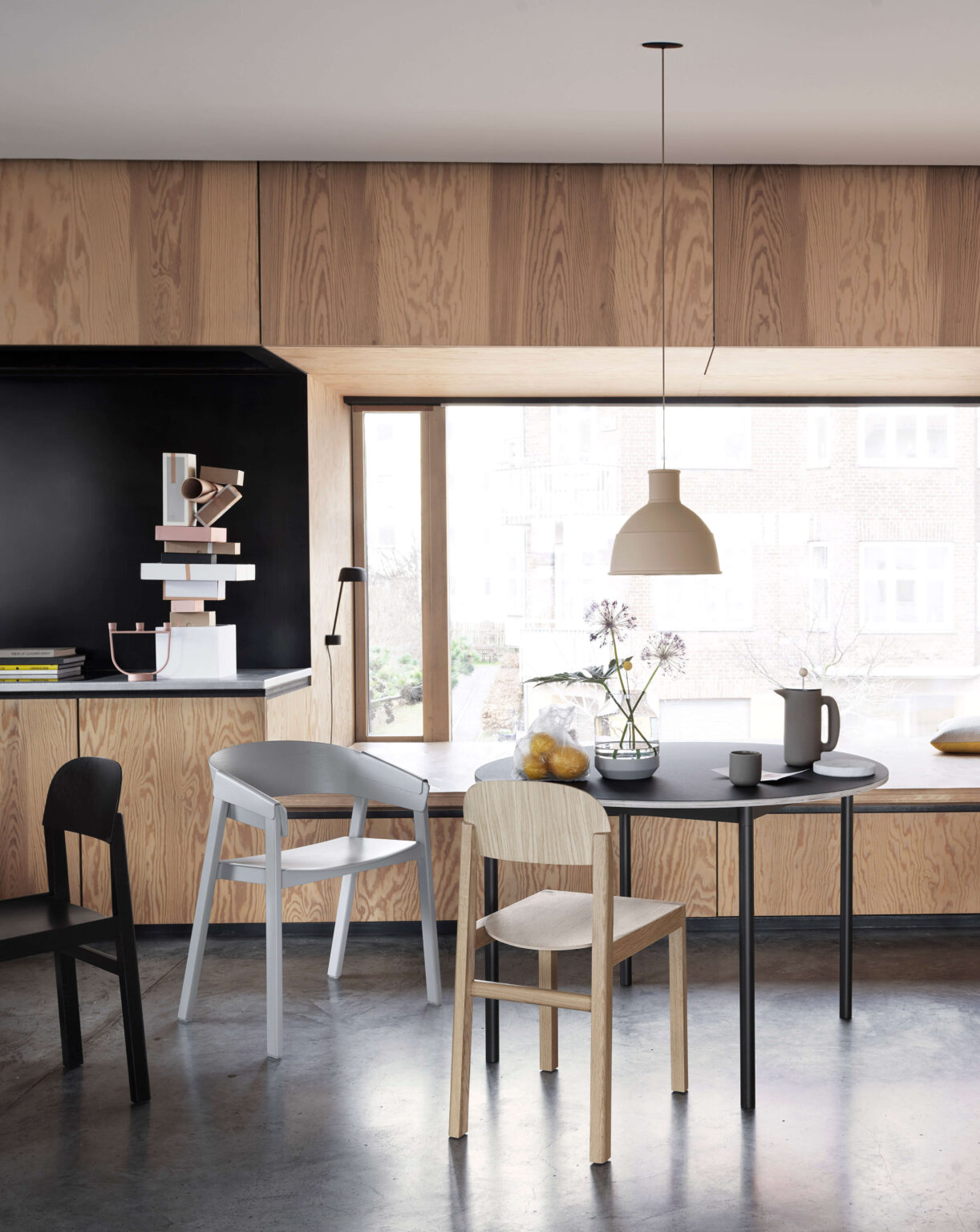 Helle Wohnküche mit Holzfronten und schwarzer Nische, runder schwarzer Esstisch mit gemischten Stuhlen, Pendelleuchte und grossem Fenster mit Tageslicht.