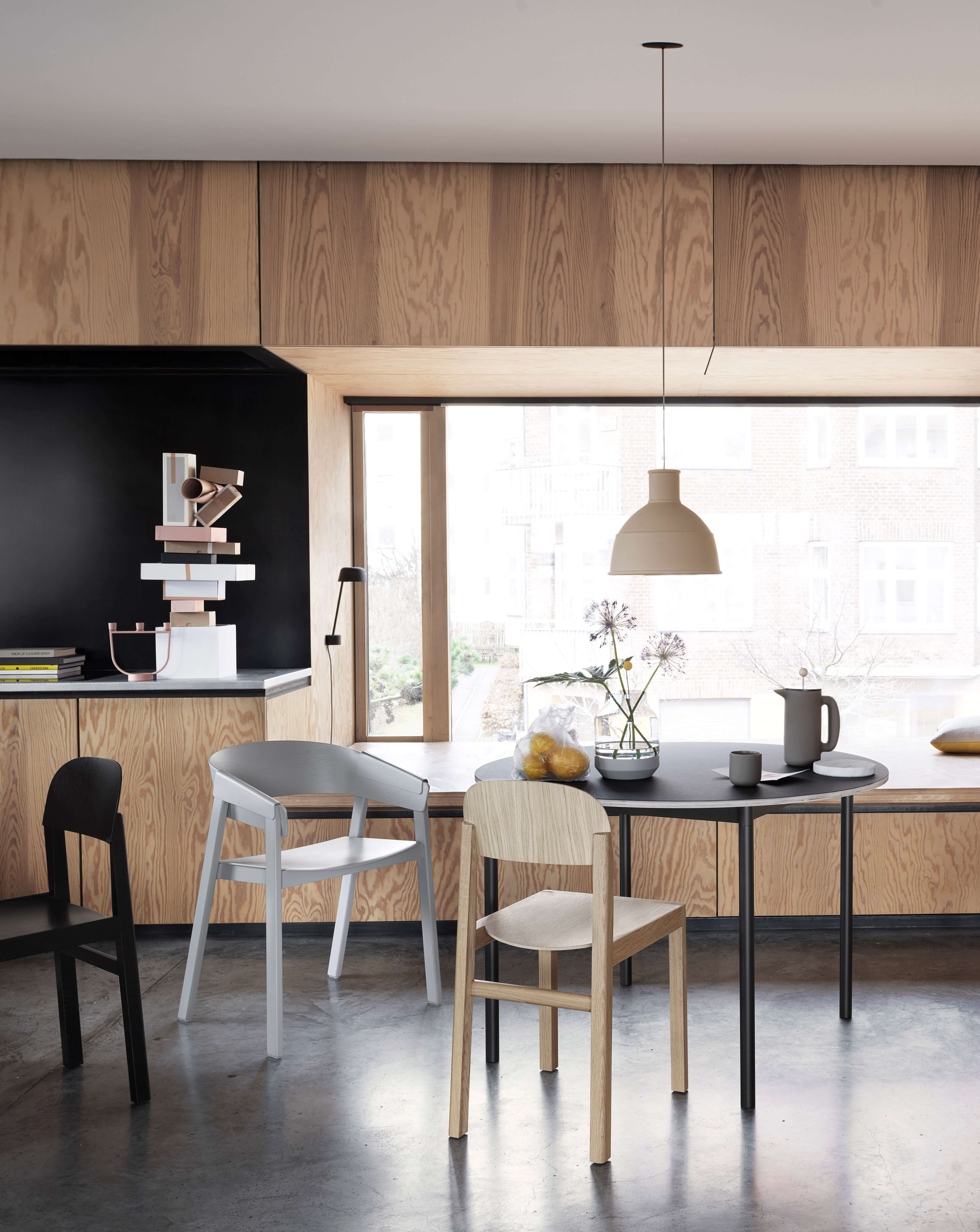 Helle Wohnküche mit Holzfronten und schwarzer Nische, runder schwarzer Esstisch mit gemischten Stuhlen, Pendelleuchte und grossem Fenster mit Tageslicht.