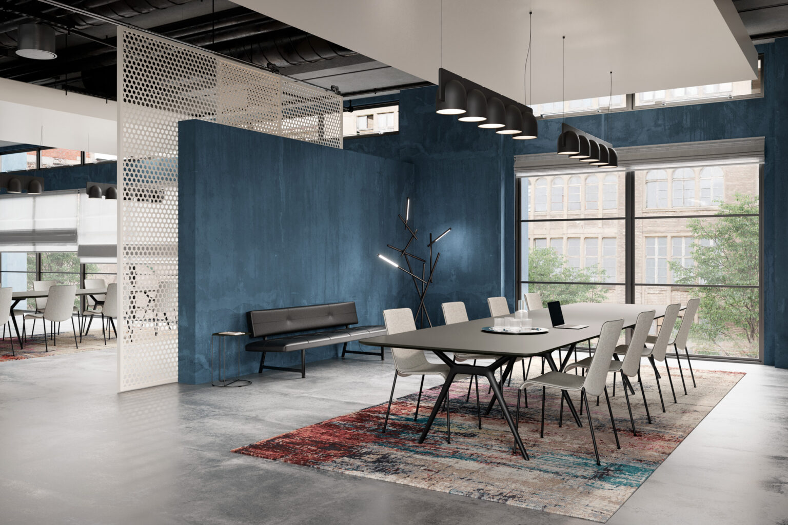 Konferenzbereich mit langem Tisch und zwölf Stühlen auf einem gemusterten Teppich. Blaue Trennwand, weisse Lochwand, schwarze Pendelleuchten, Bank mit Beistelltisch und skulpturaler Stehleuchte vor grossen Fenstern im Industrial Look.