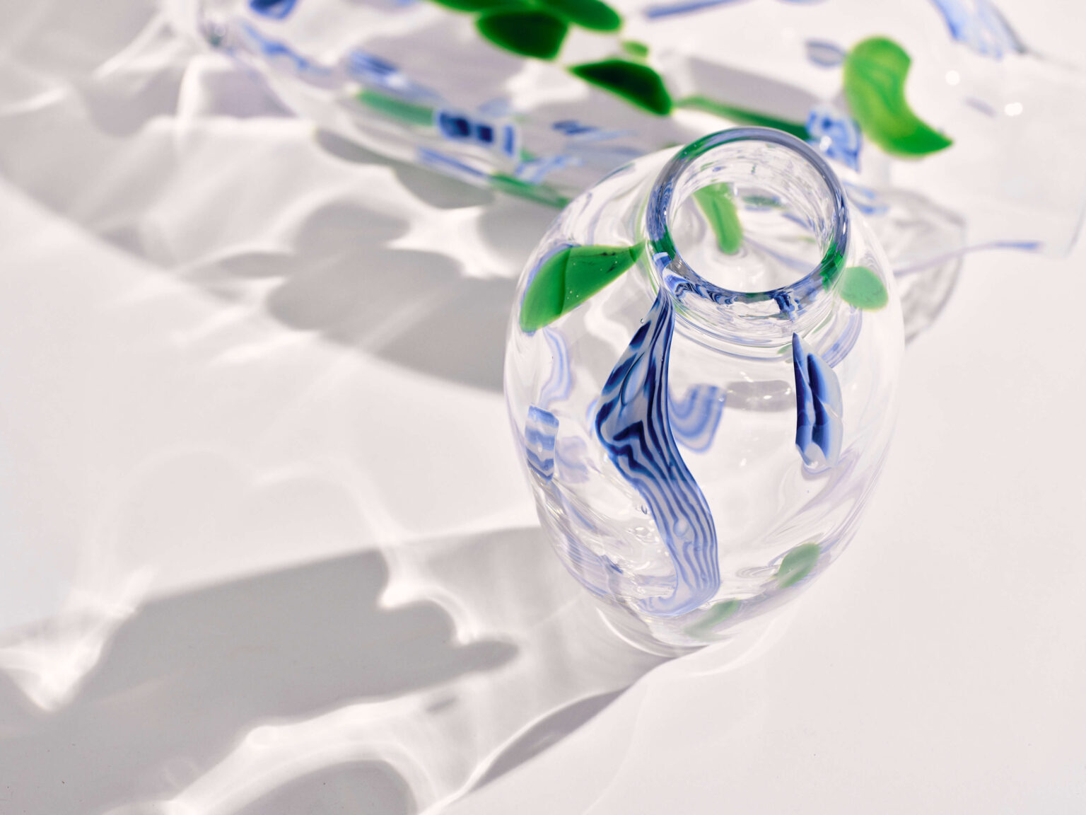 Transparente Glasvase mit grünen und blauen Einschlüssen im Licht.