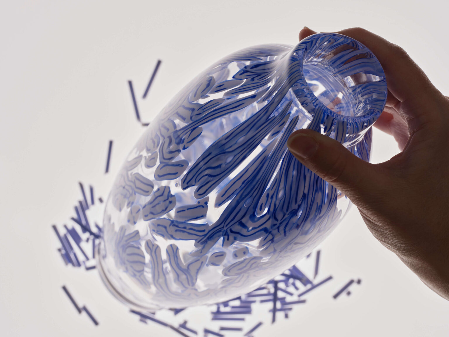 Hand hält transparente Glasvase mit blauen Mustern.