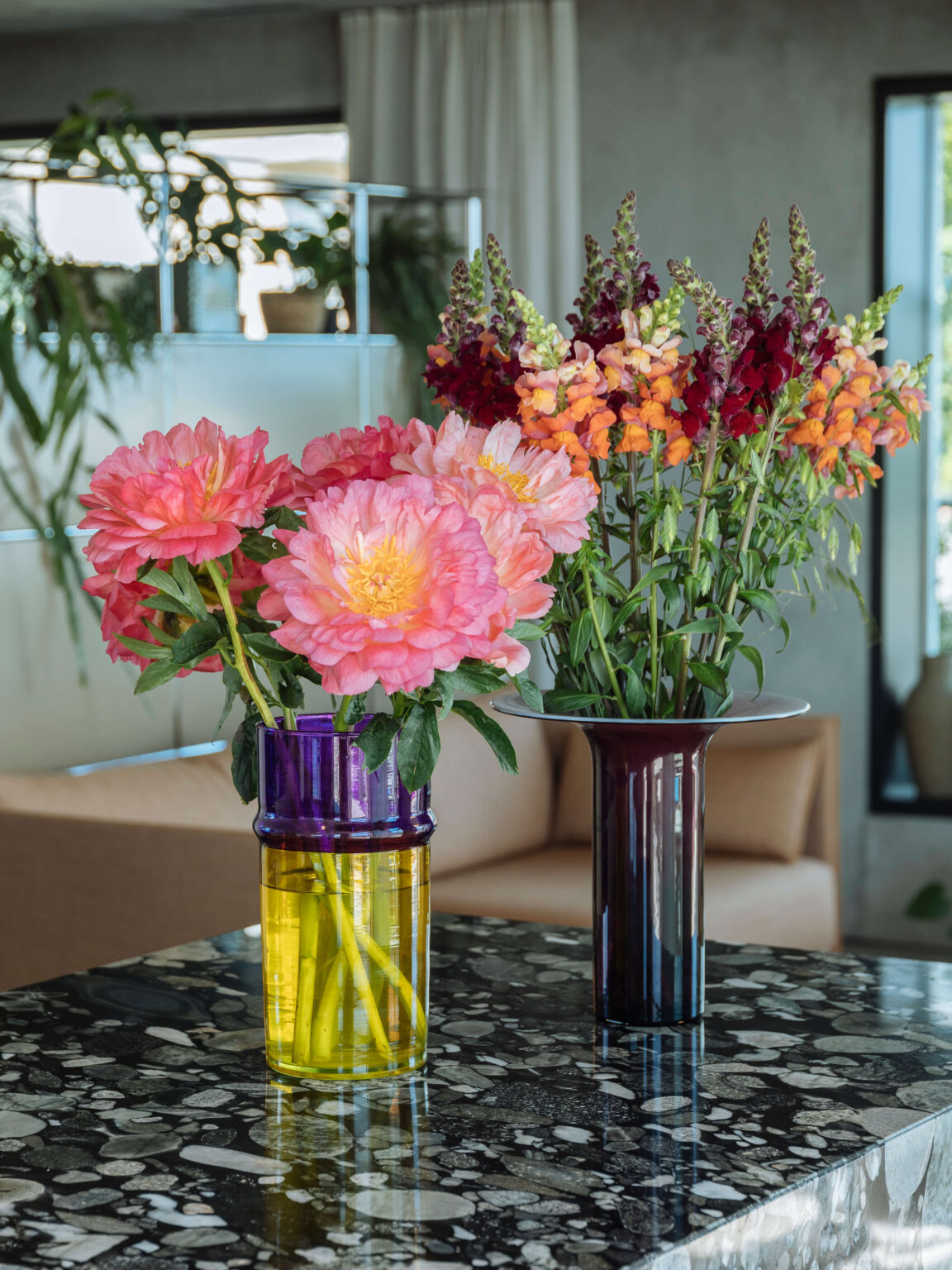 Zwei Vasen mit farbigen Blumen auf dunkler Steinoberfläche.
