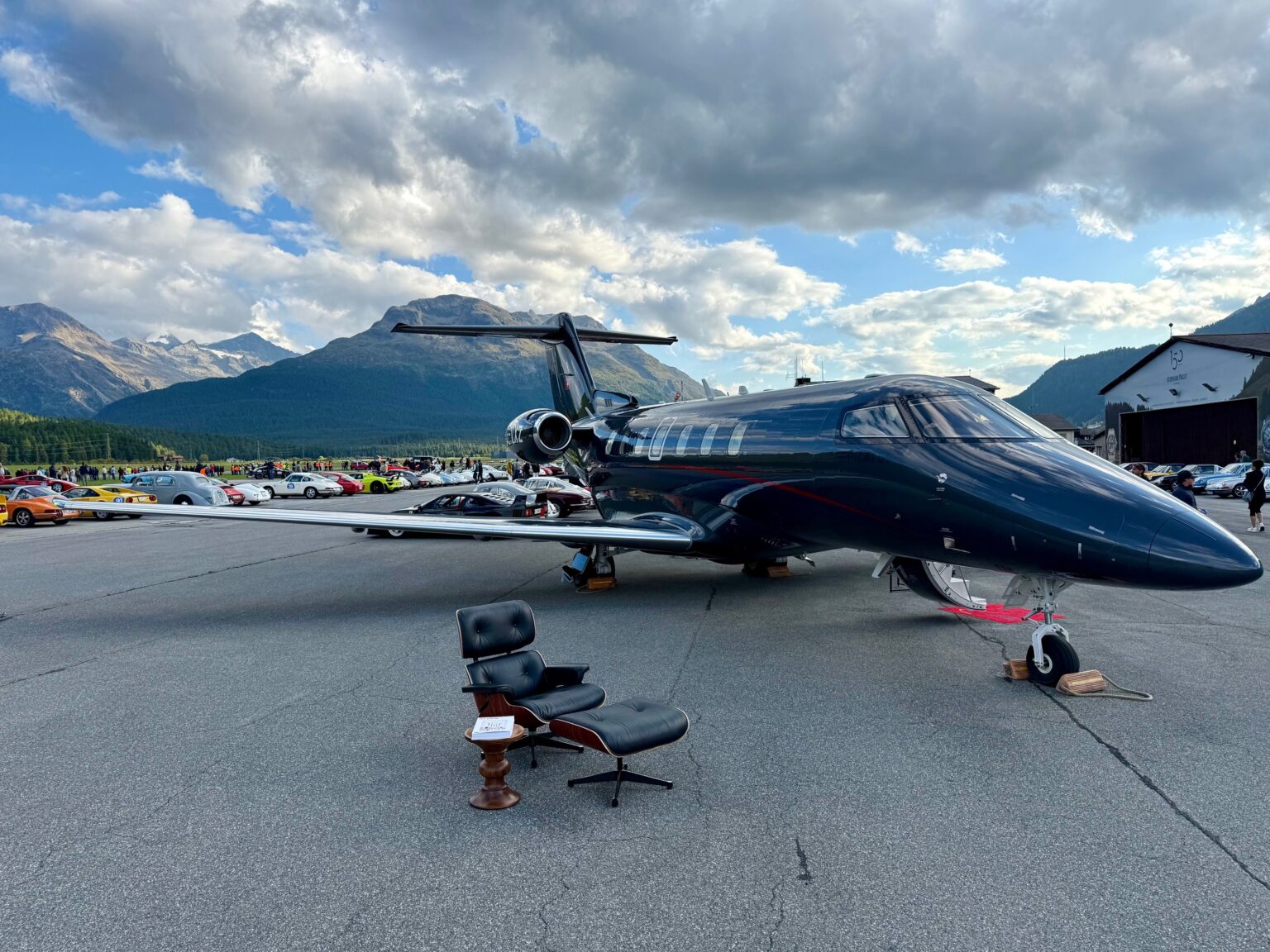 Privatjet auf Rollfeld vor Alpenkulisse mit Lounge Sessel im Vordergrund.