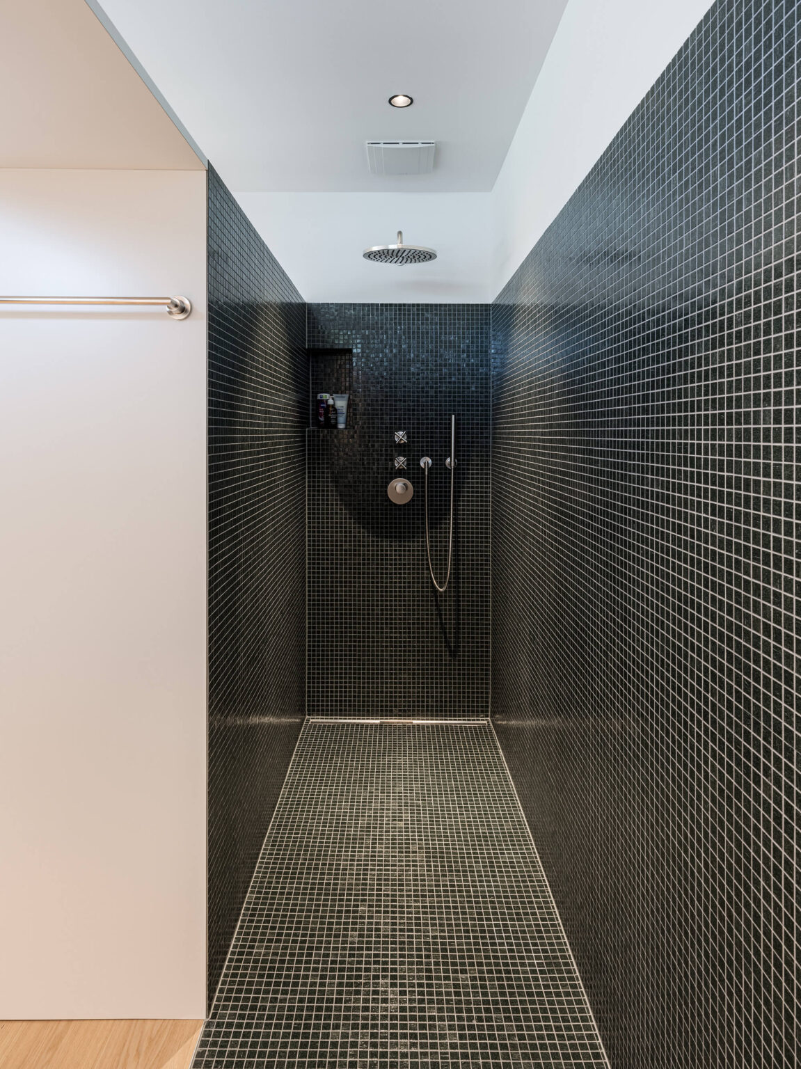 Begehbare Dusche mit dunklen Mosaikfliesen und Regendusche.