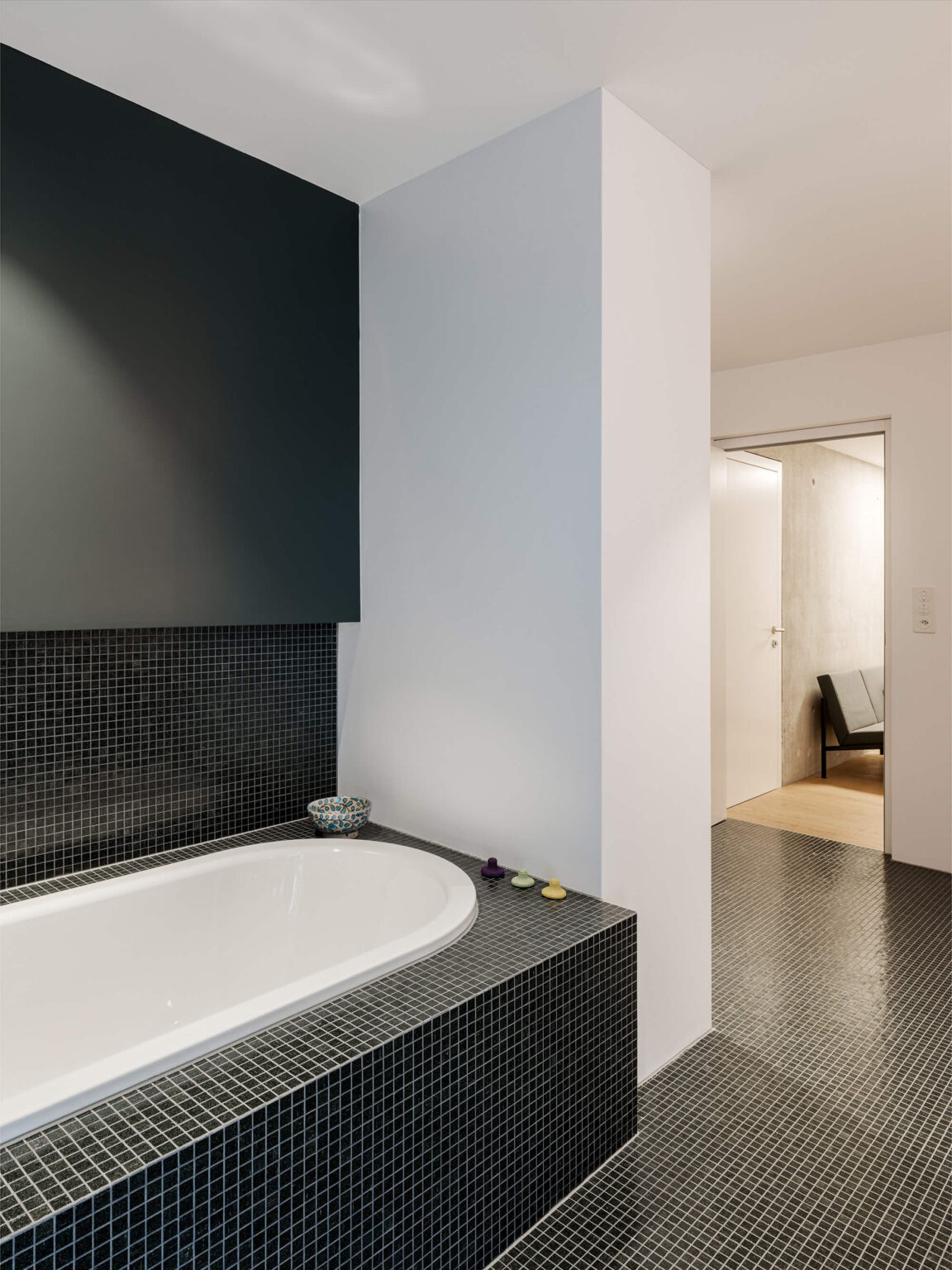 Badezimmer mit eingelassener Badewanne und dunklen Mosaikfliesen.
