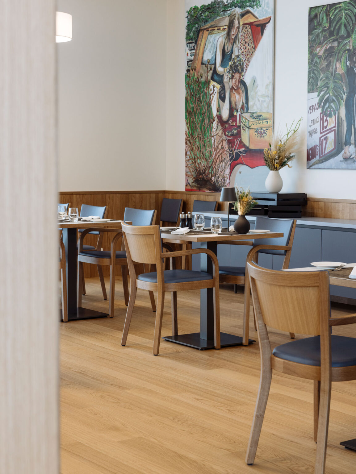 Restaurantbereich mit Holztischen und Stühlen vor grossformatigem Wandbild.