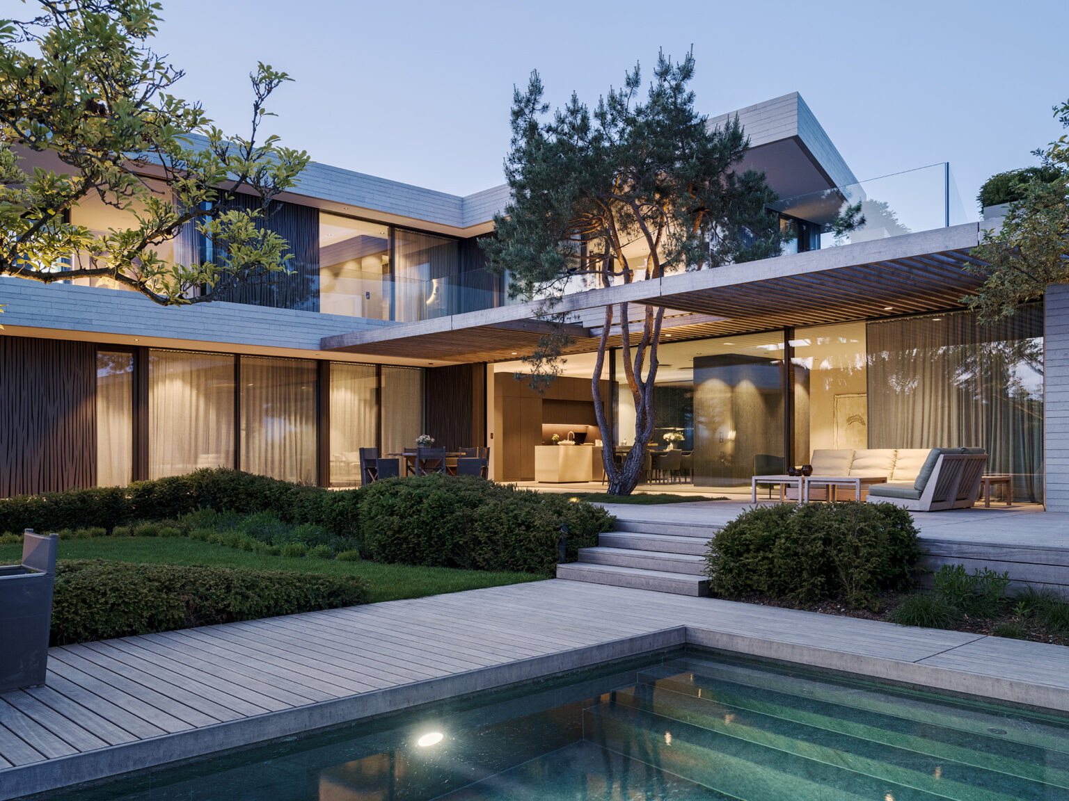 Modernes Privathaus mit Pool, Gartenanlage und weit auskragender Pergola vor grossen Glasfronten.