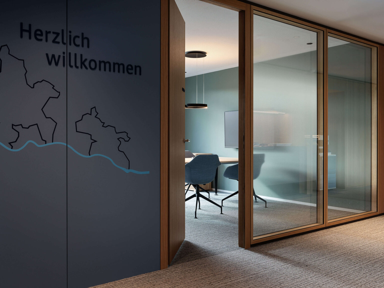Meetingraum mit grüner Akzentwand, Holz Tür und Sideboard.