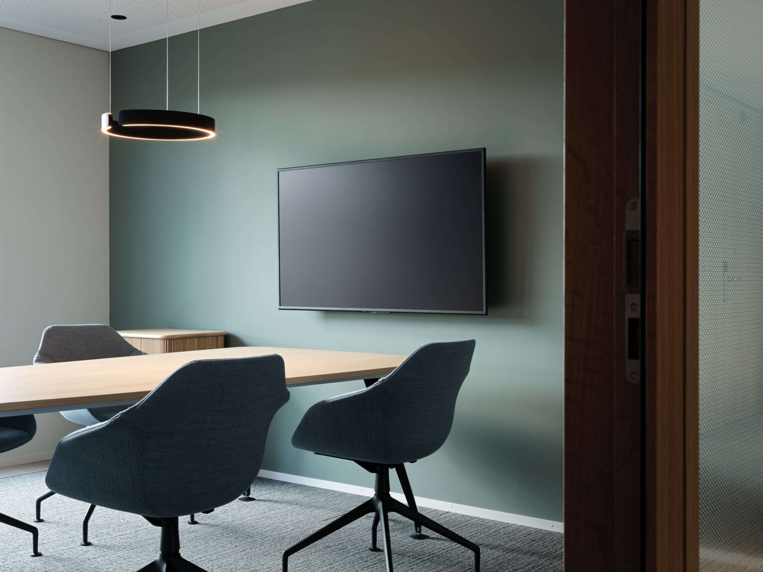 Meetingraum mit grüner Akzentwand, Holz Tür und Sideboard.