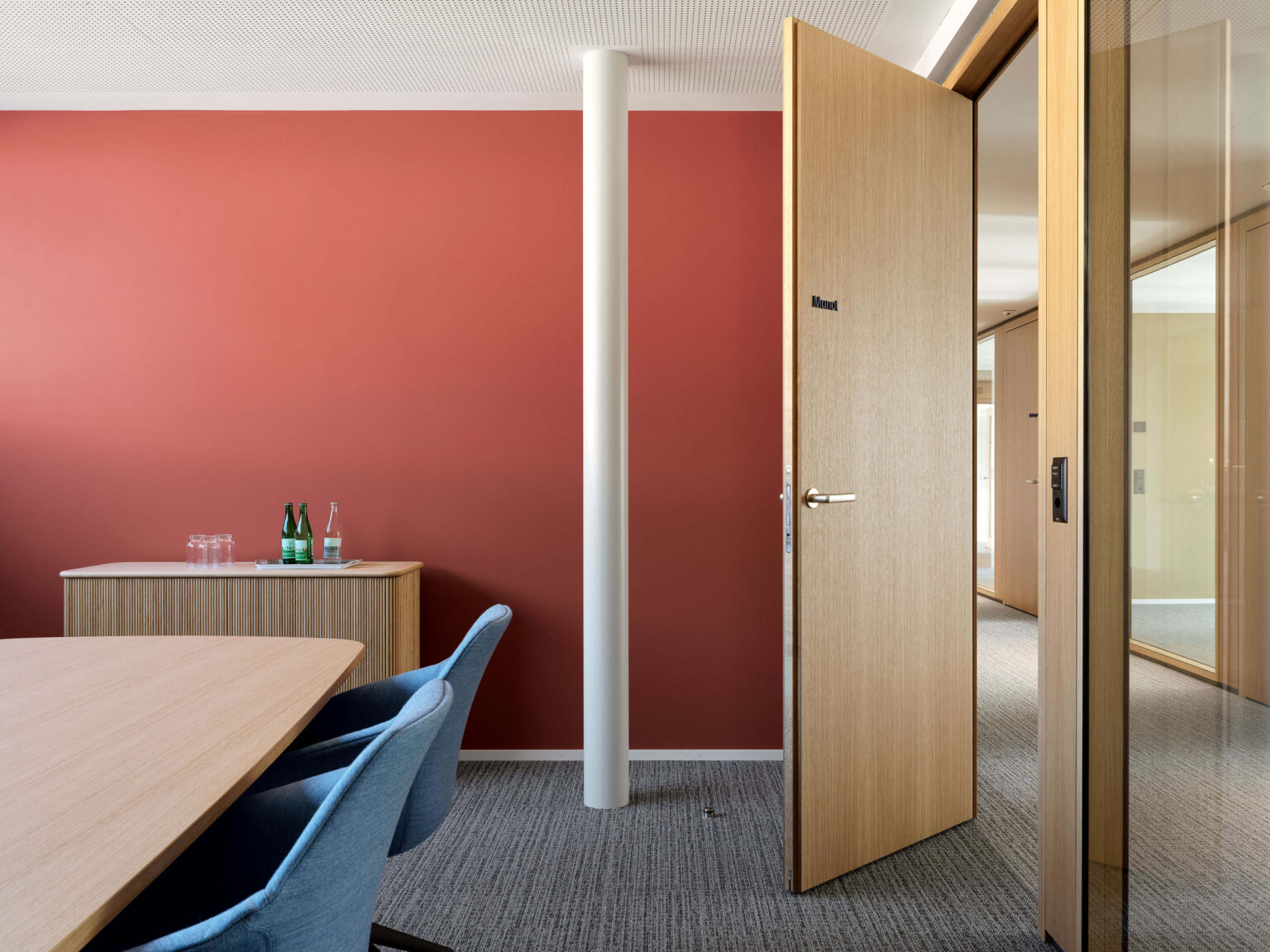 Meetingraum mit roter Akzentwand, Holz Tür und Sideboard mit Wasserflaschen und Gläsern.