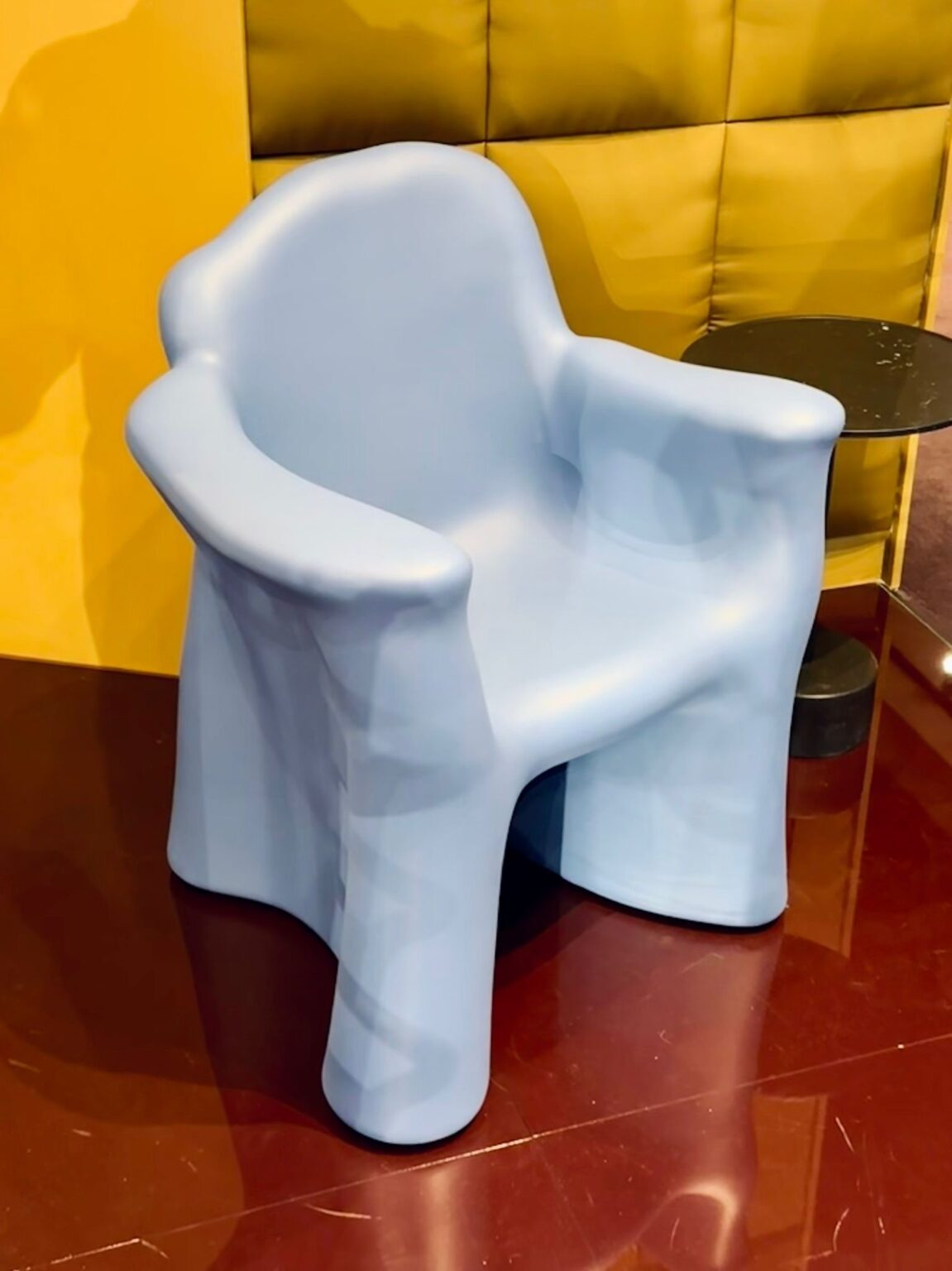 Skulpturaler Kunststoff Sessel in Hellblau vor gelber Wand.