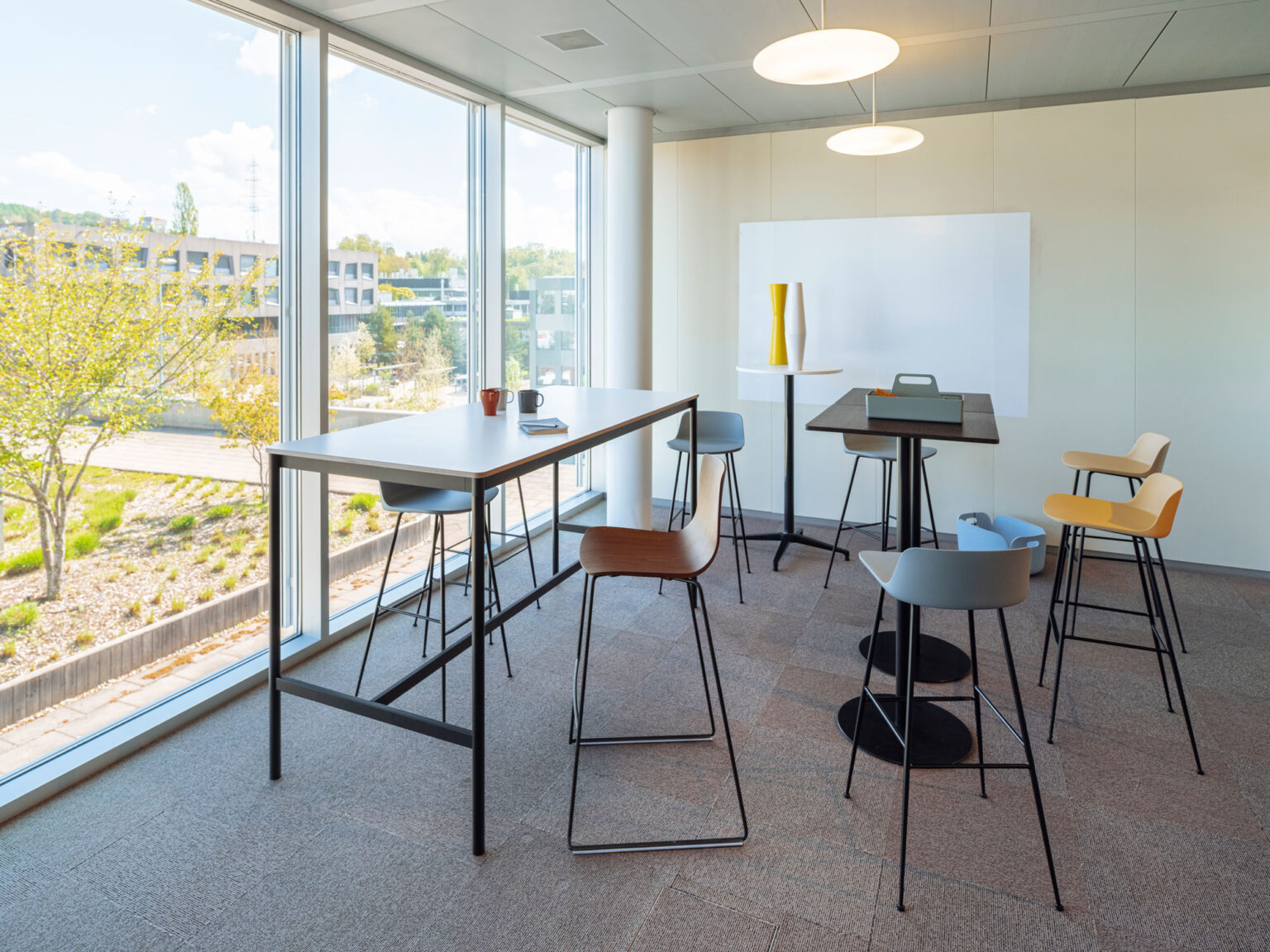 Moderner Meetingbereich mit Hochtischen und grossen Fensterflächen.