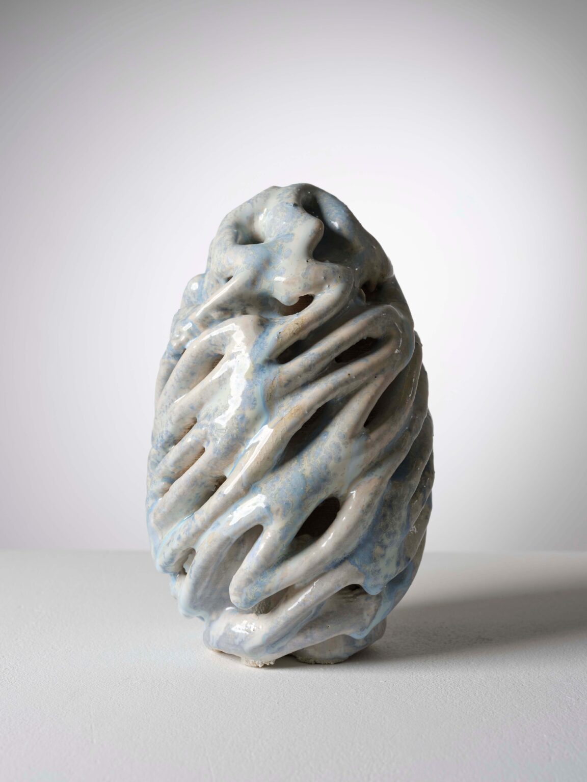 Organische Keramikskulptur von Raphaël Emine mit glänzender, hellblauer und cremefarbener Glasur, durchbrochener Struktur und fliessenden Formen.