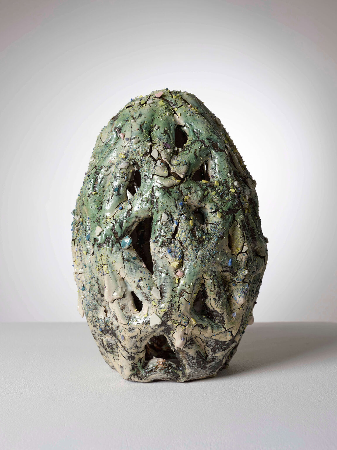 Eiförmige Keramikskulptur von Raphaël Emine mit grüner Glasur, dunklen Rissen, farbigen Einschlüssen und durchbrochener Oberfläche.