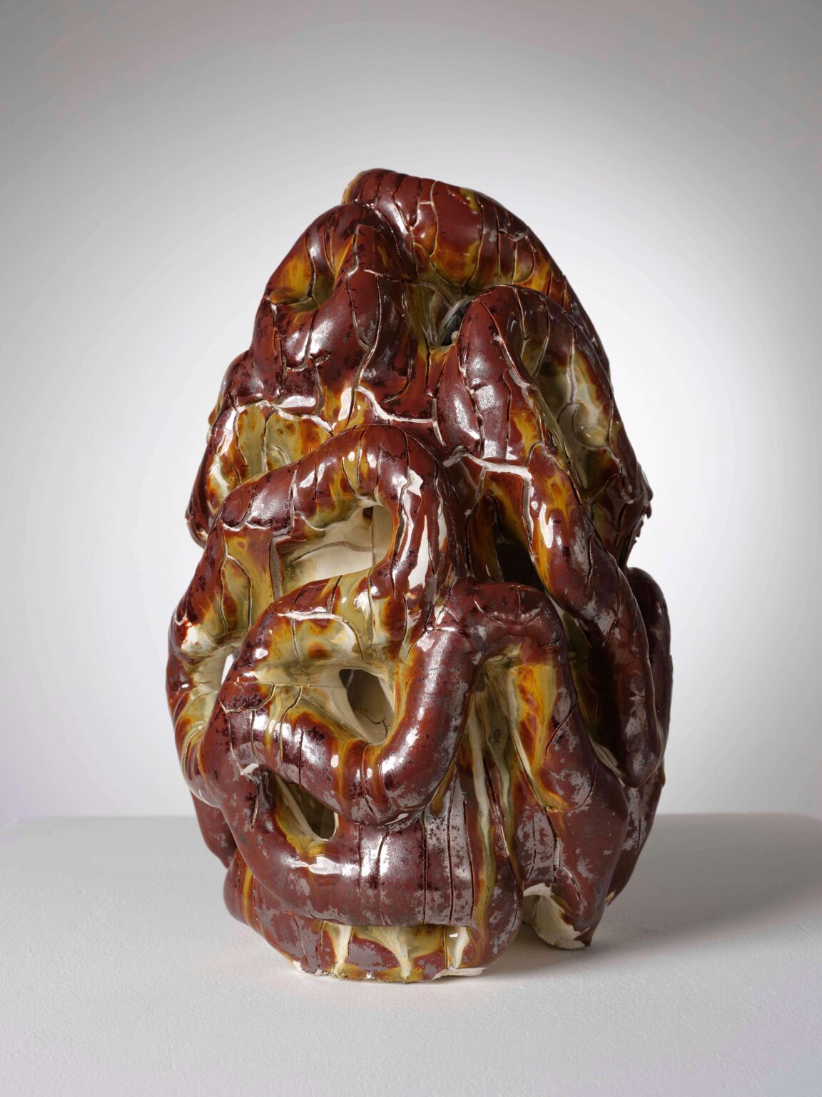 Organische Keramikskulptur von Raphaël Emine mit glänzender rotbrauner Glasur, gelblichen Verläufen und durchbrochener, verschlungener Struktur.