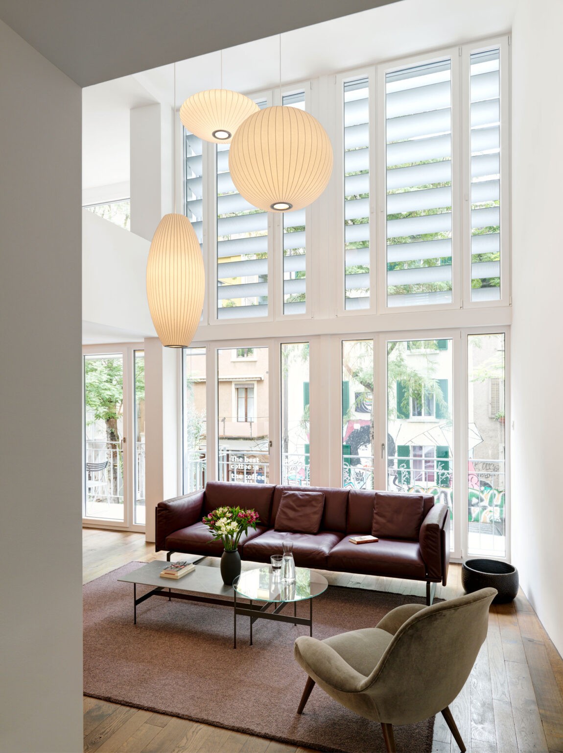 Helles Wohnzimmer mit braunem Ledersofa, grossen Fensterfronten und Papierpendelleuchten.