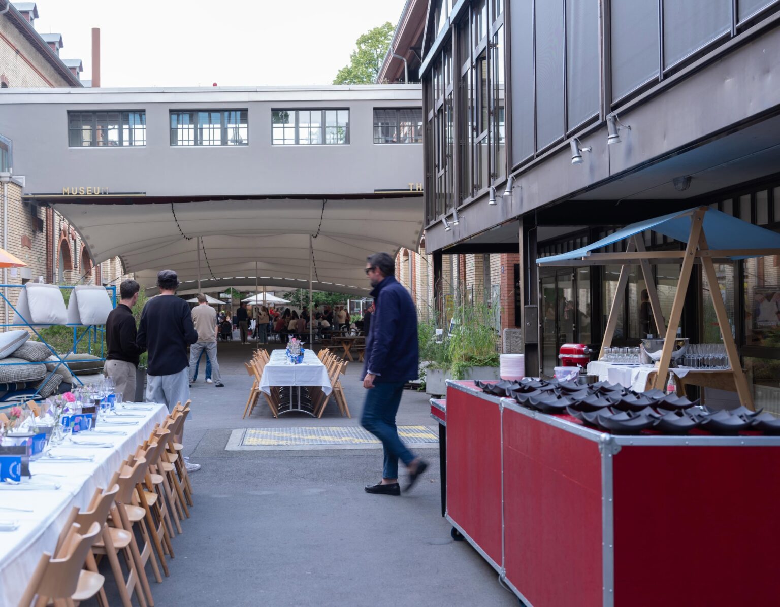 Aussenbereich des Pop up Restaurants in der Mühle Tiefenbrunnen bei teo jakob Zürich mit langen gedeckten Tafeln, Servicebereich und Gästen im urbanen Innenhof.