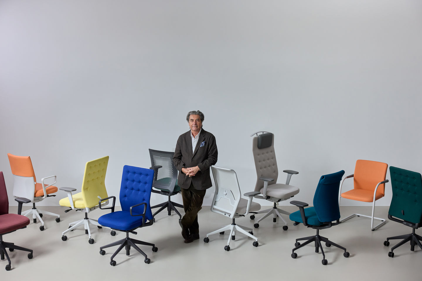 Person steht zwischen verschiedenen farbigen Vitra Bürostühlen mit unterschiedlichen Rückenlehnen, Polsterungen und Gestellen in einem reduzierten Studio Setting.