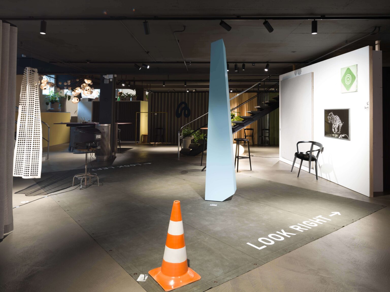 Ausstellungsfläche bei teo jakob Bern mit Abbey Stuhl von horgenglarus, Kunstwerken, Lichtobjekten, blauem Raumkörper und Verkehrskegel im Eventsetting.